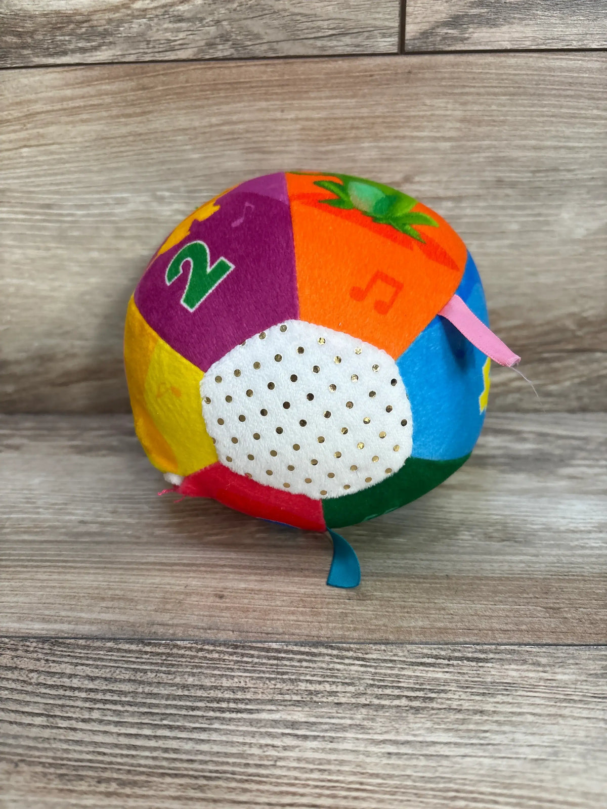 Front view of Move2Play Interactive Soft Ball showcasing colorful plush panels, musical notes, and a textured white panel with ribbons