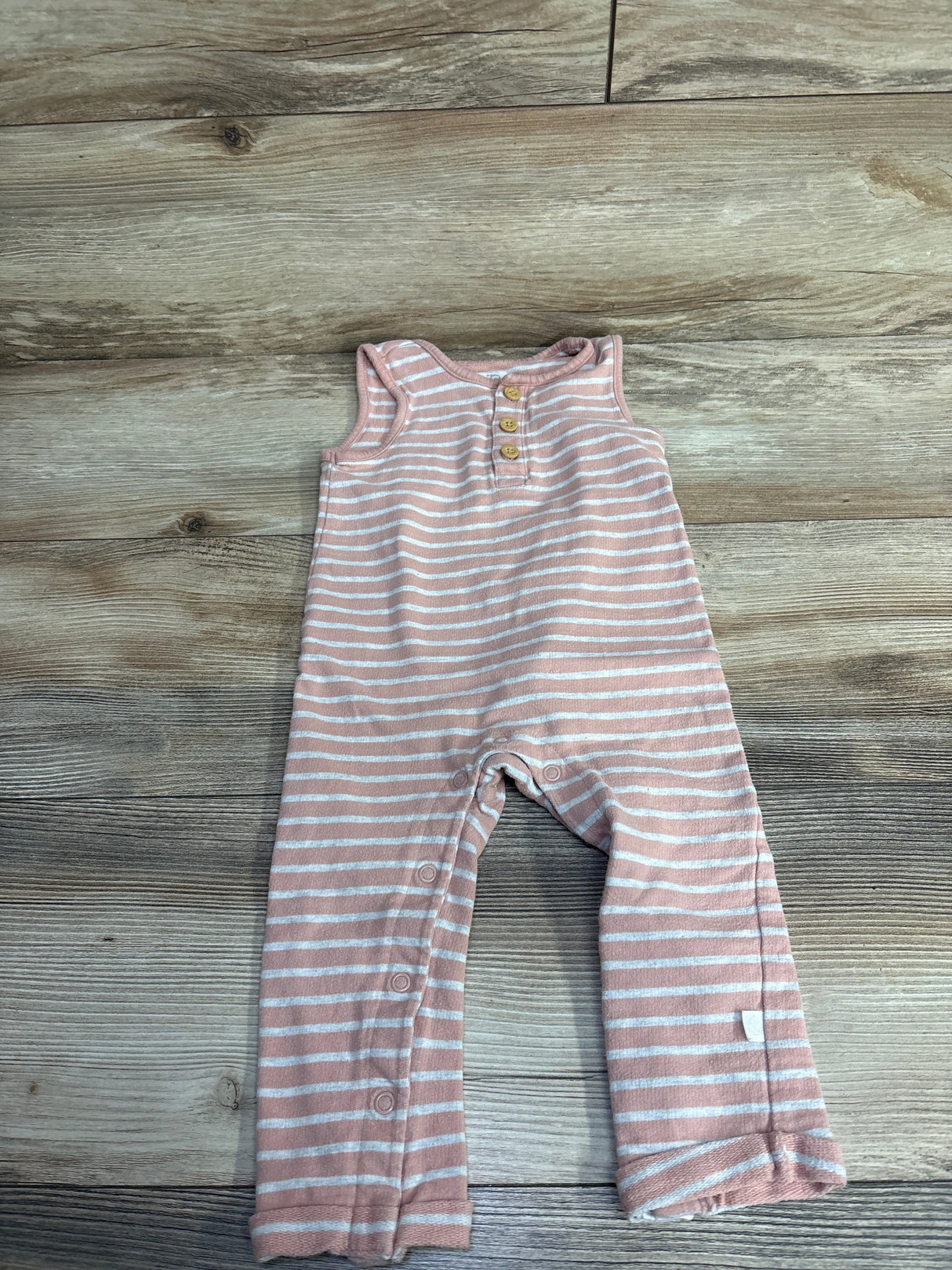 Pink and white striped sleeveless baby romper with buttons on front and snaps along legs on wood floor