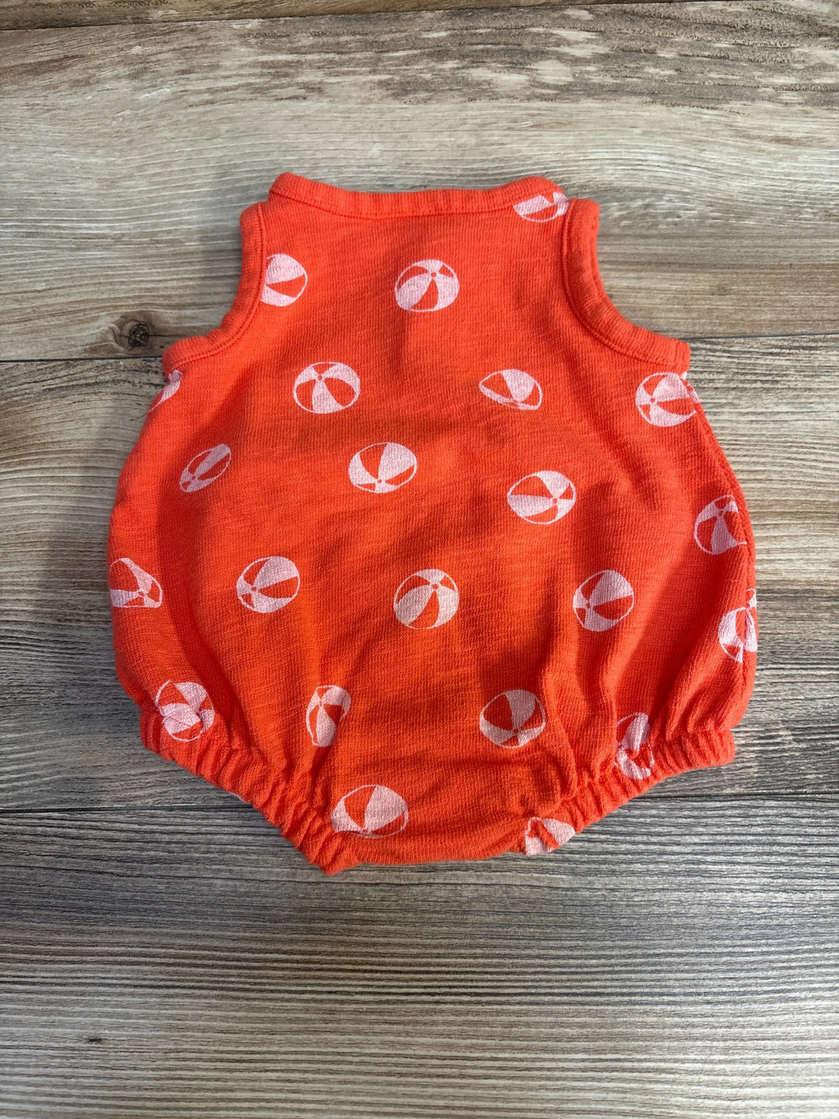 Flat lay back view of orange newborn romper with white beach-ball print and elasticized leg openings on wood background