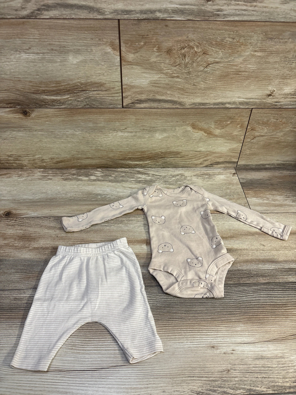 Flat lay of Carter’s newborn 2-piece beige bear bodysuit and striped pants set showcasing bear face print on bodysuit with wood plank background
