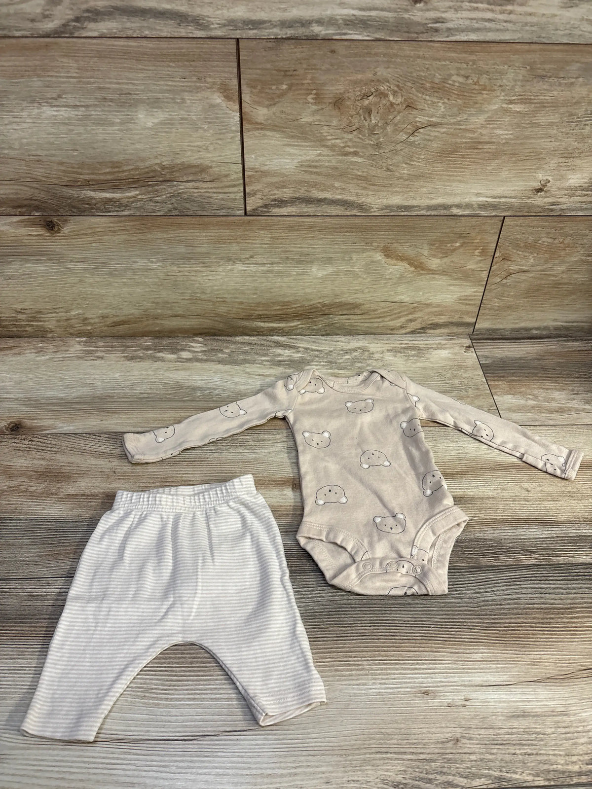 Flat lay of Carter’s newborn 2-piece beige bear bodysuit and striped pants set showcasing bear face print on bodysuit with wood plank background