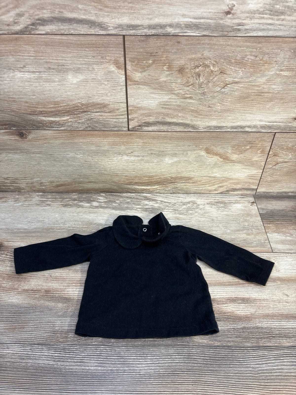 Front view of Cat and Jack collared shirt in black, size 0 to 3 months, showcasing long sleeves and rounded collar on wood flooring
