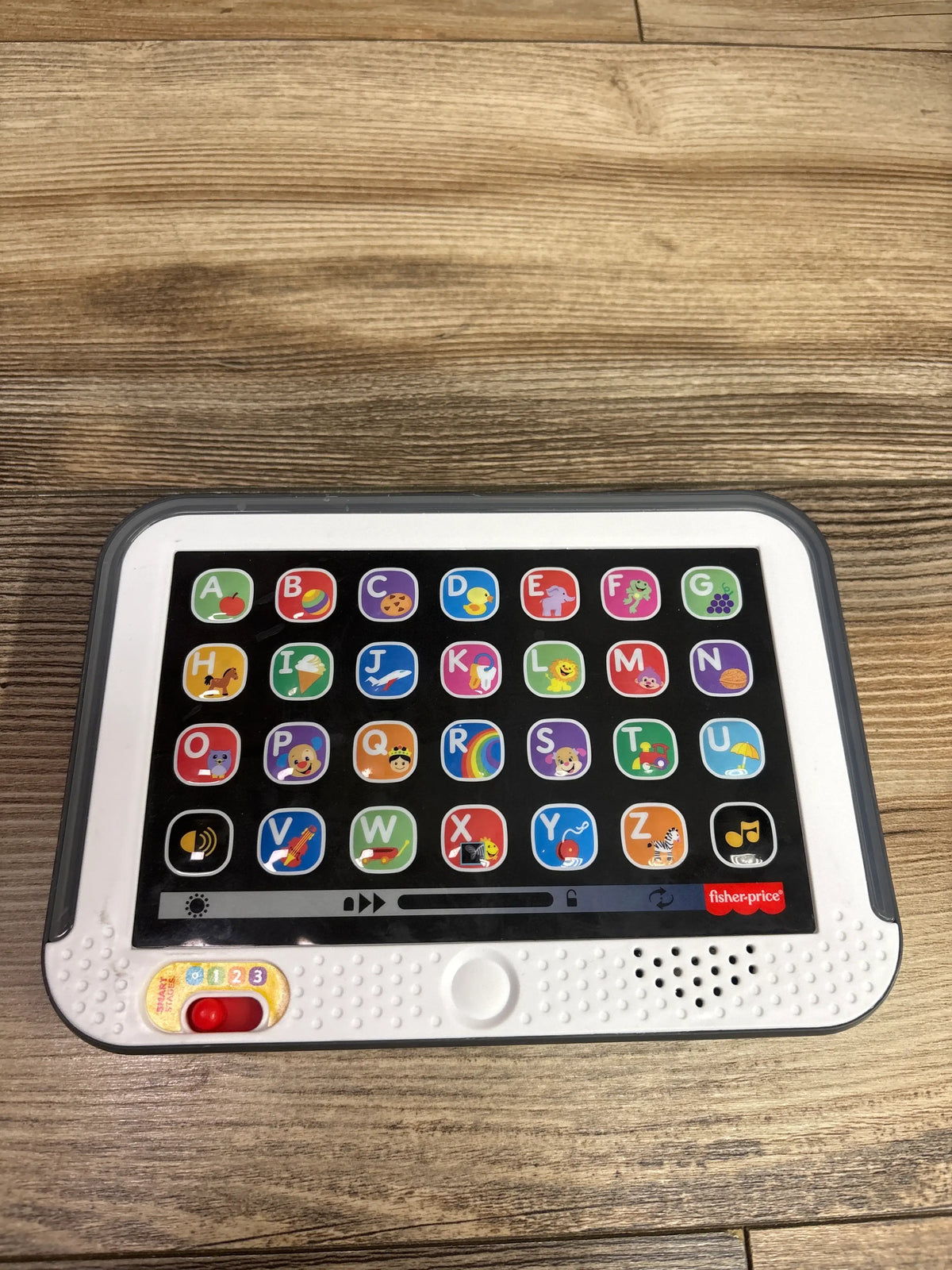 Front view of Fisher Price Laugh & Learn Smart Stages Tablet showcasing alphabet buttons and numbered switch on a wood surface