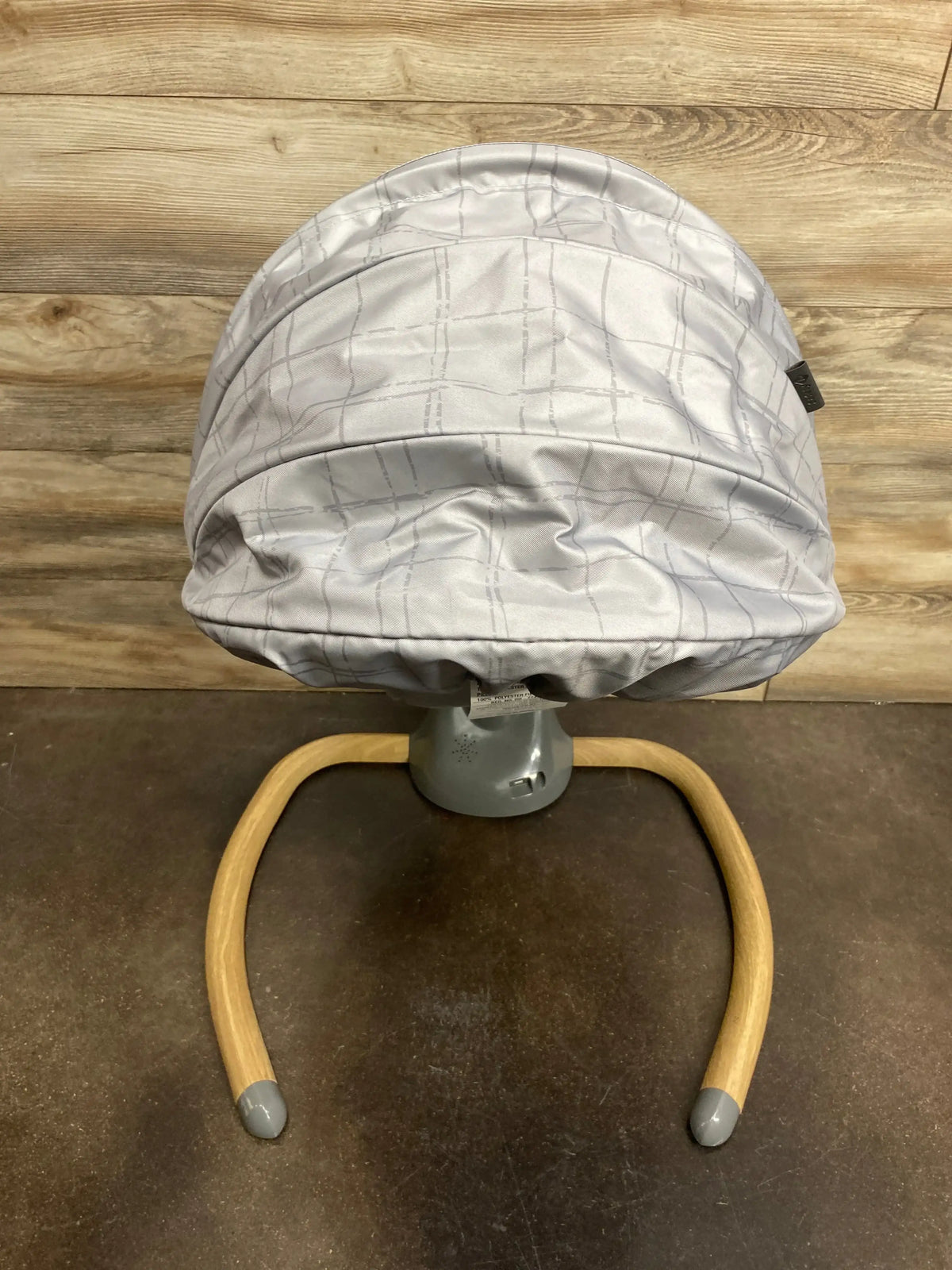 Modern baby bouncer with light gray fabric seat and wooden legs on wood floor