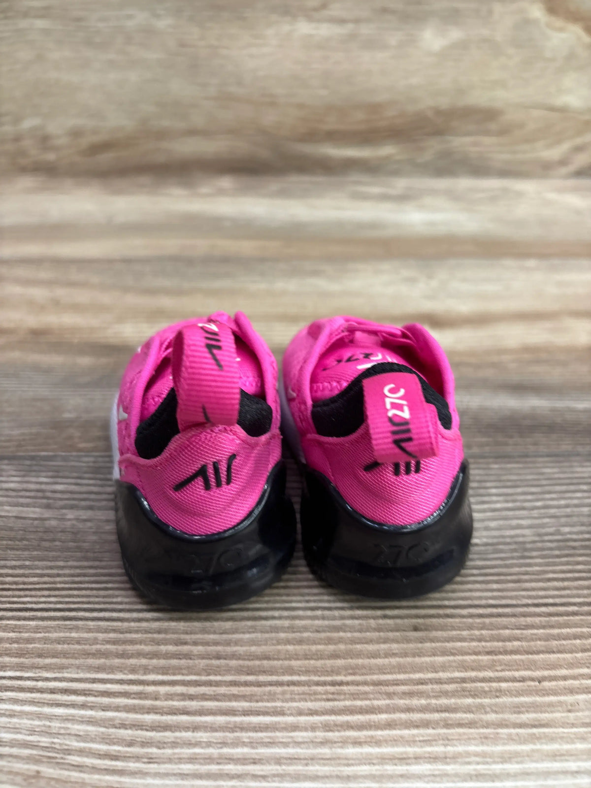 Rear view of Nike Air Max 270 TD Laser Fuchsia sneakers in size 2C showcasing pink uppers and black soles on a wood surface