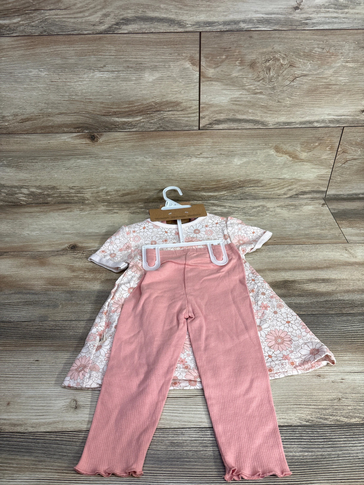 Children's outfit with floral dress and pink ribbed leggings on wooden floor background
