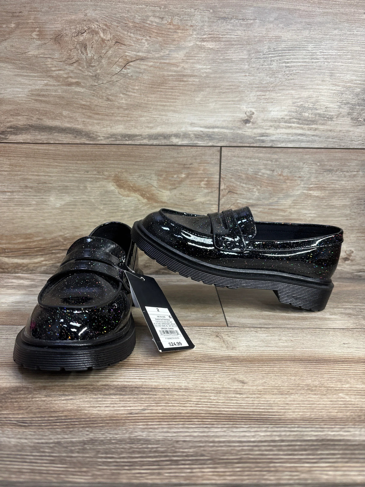 Black glittery kids' loafers with chunky soles and price tag on wood background