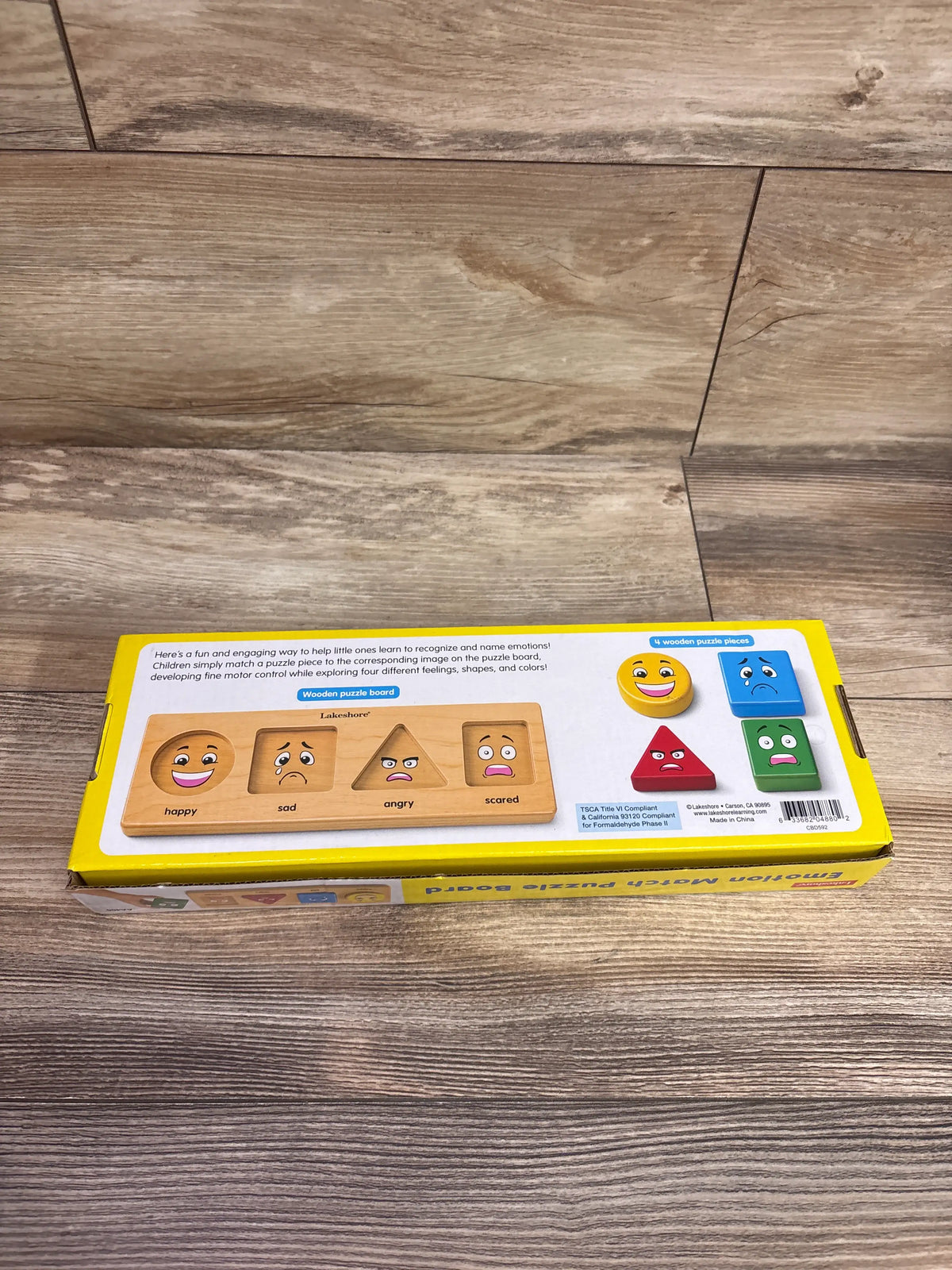 Lakeshore Emotion Match Puzzle Board with happy, sad, angry and scared faces plus four colored pieces on a wood floor