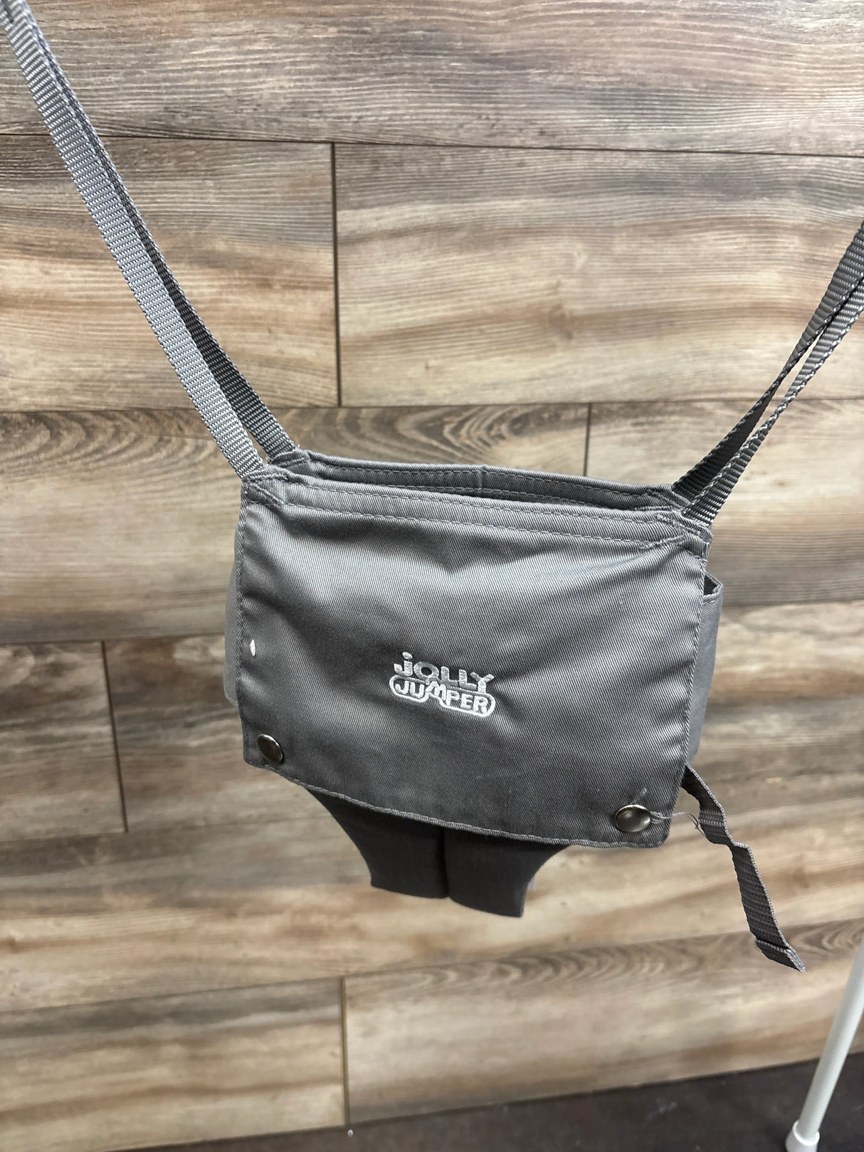 Front view of Jolly Jumper seat in grey showing embroidered logo, hanging from straps with part of metal stand visible