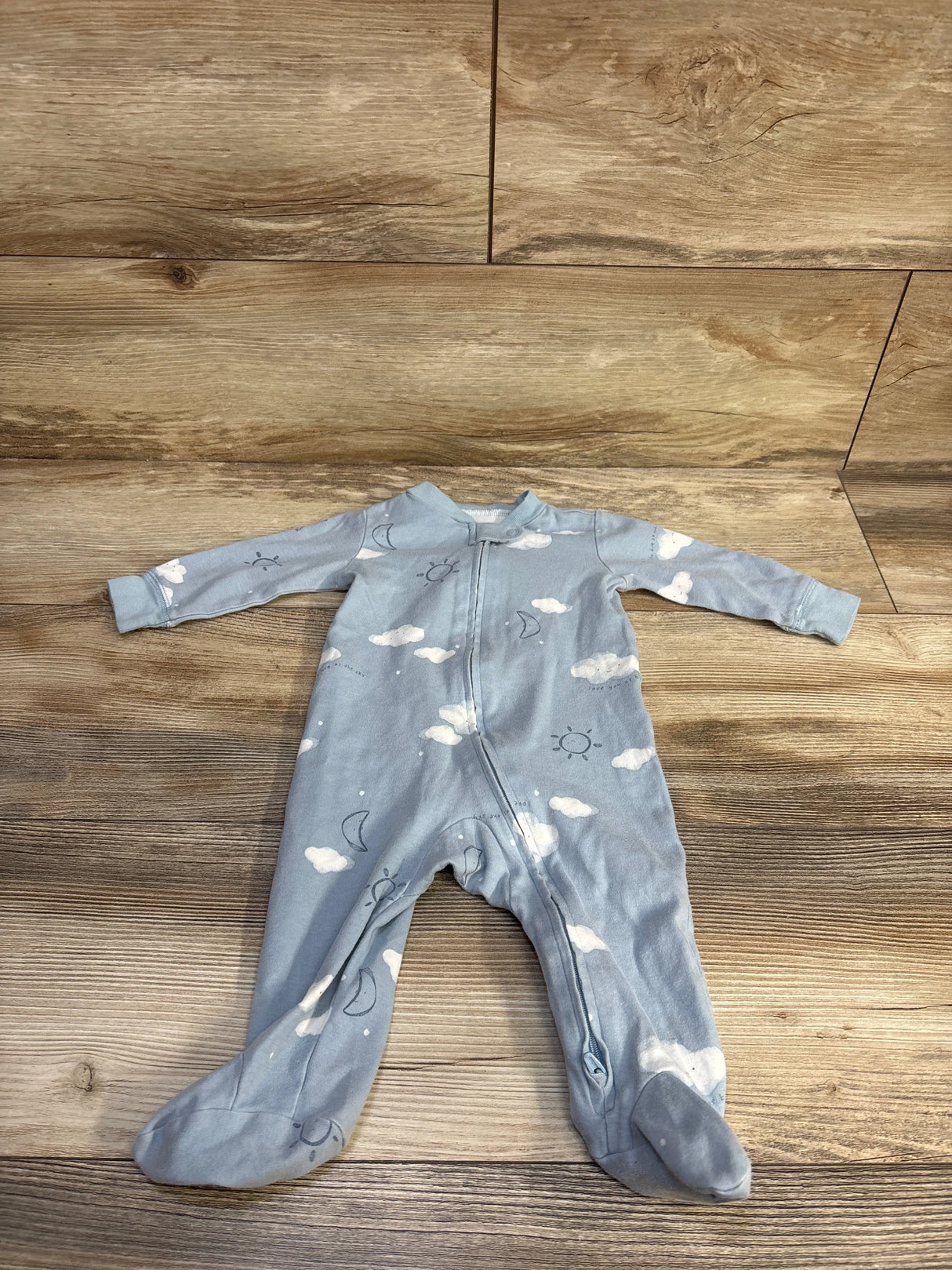 Front view of blue Carter’s footed sleeper (6M) with cloud, moon, and sun print and front zipper on wood floor
