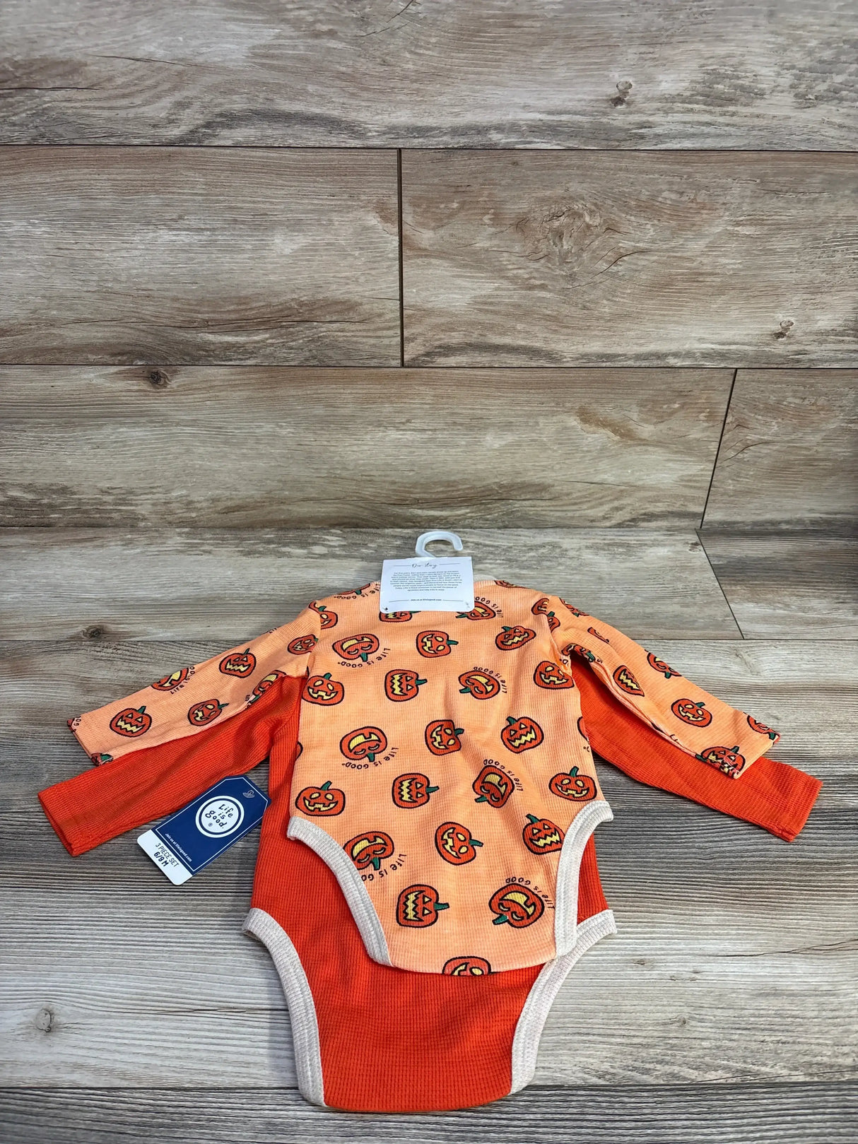 Front view of 3-piece orange pumpkin bodysuit set showcasing long sleeves and pumpkin prints on a wood-look background