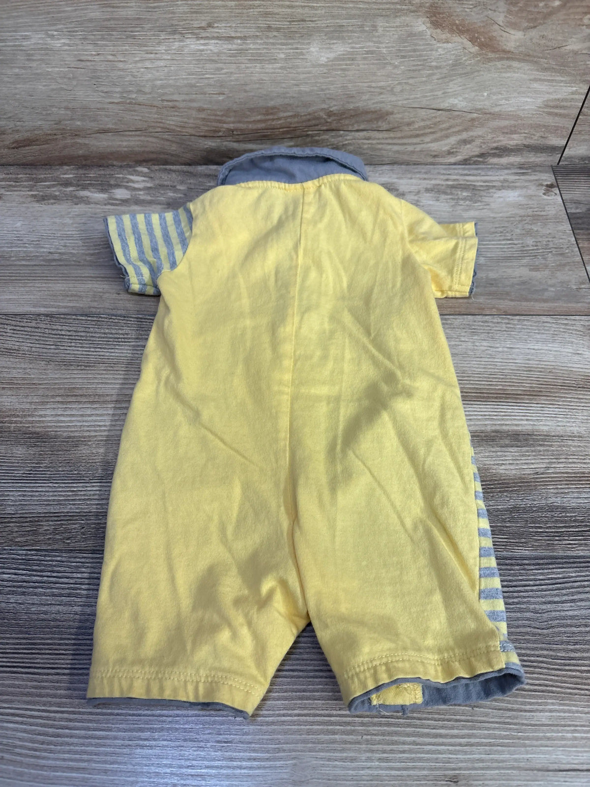 Back view of First Impressions polo shortie romper showcasing yellow cotton fabric, gray-striped sleeves and side panels, and gray collar trim on wood plank background