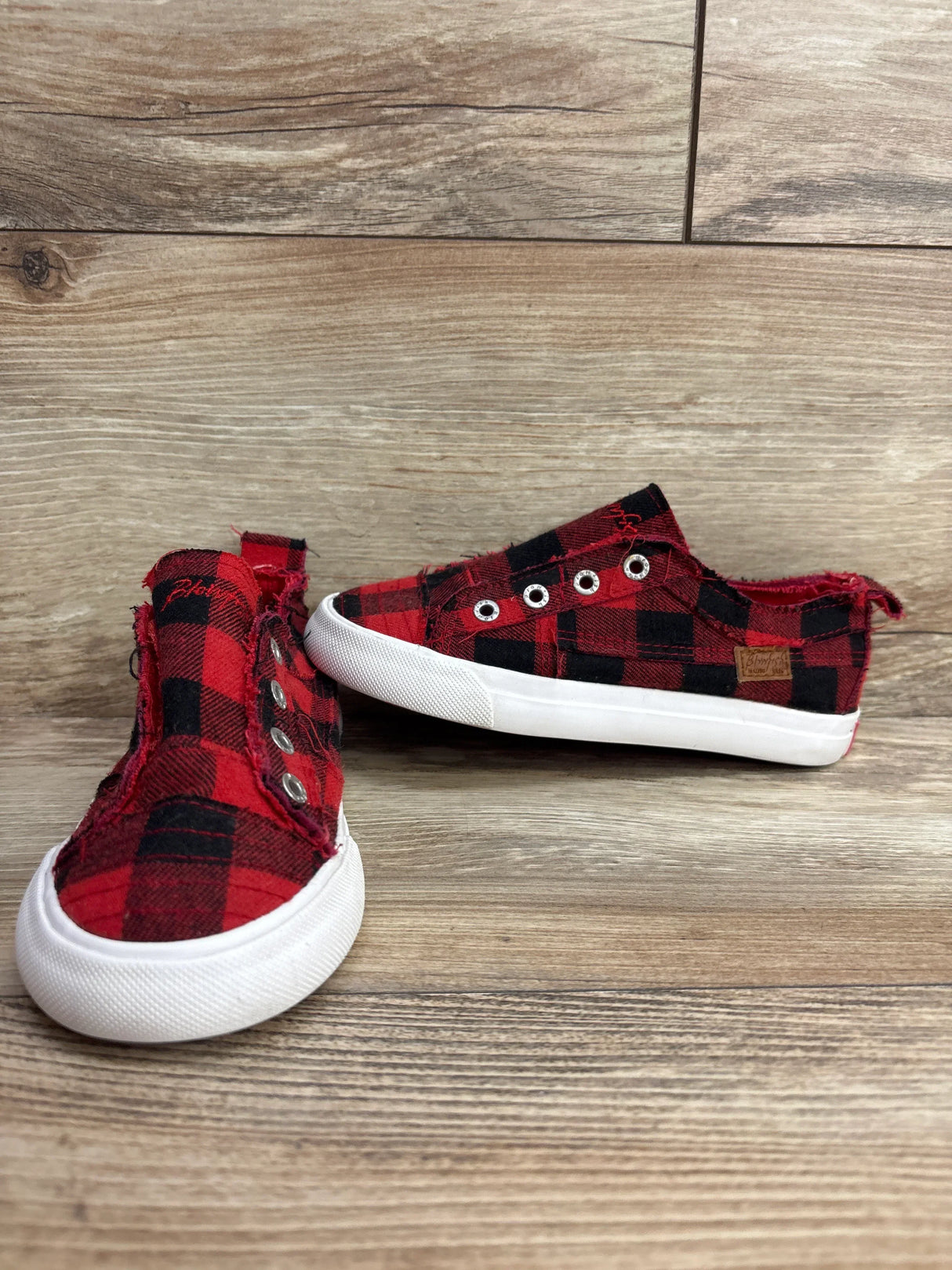 Pair of red and black plaid slip-on toddler shoes with white rubber soles on wooden surface