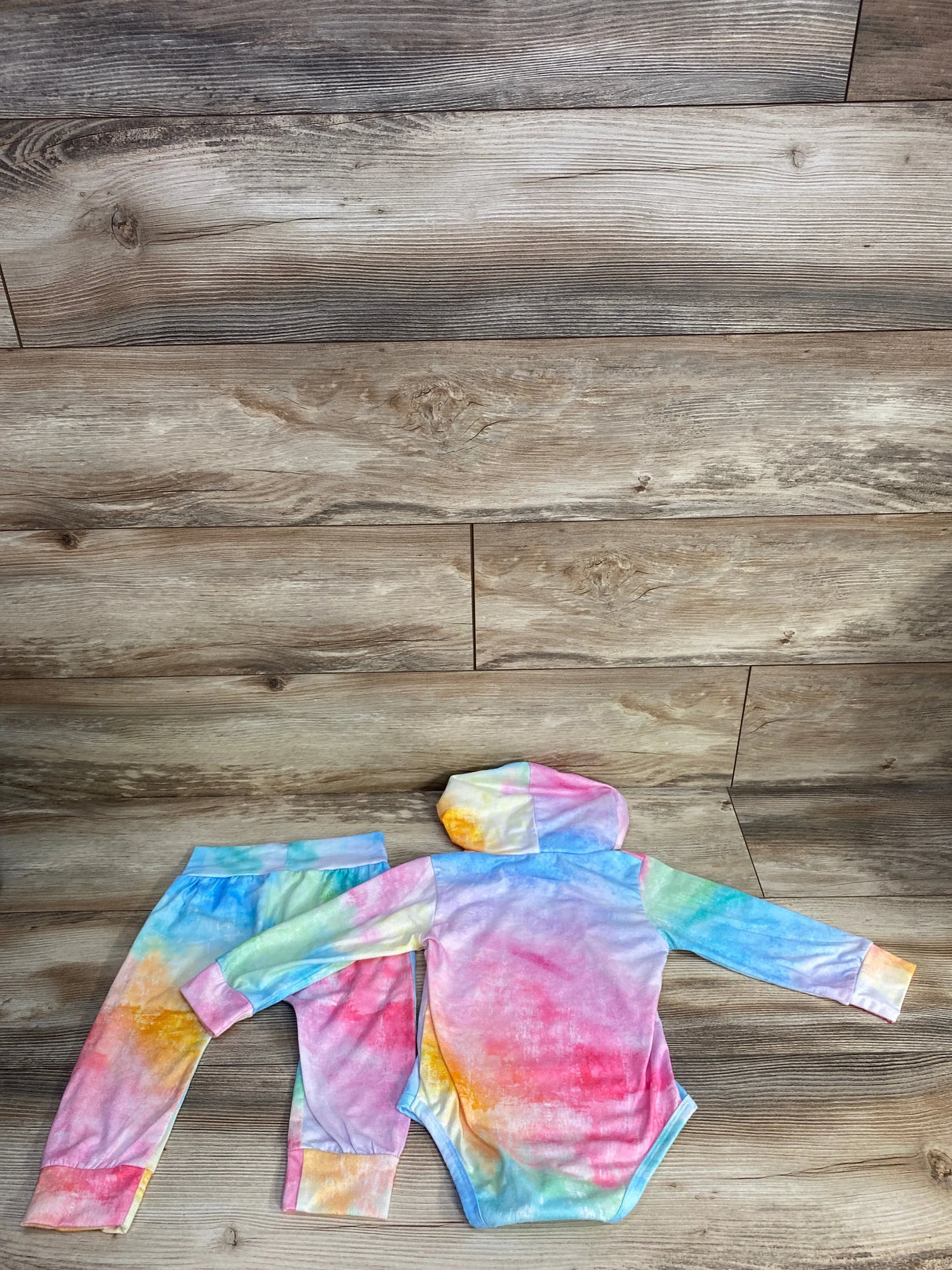 Colorful tie-dye baby hoodie bodysuit and pants set on wood background