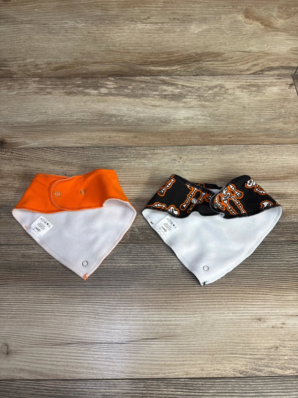 Orange and black skeleton print baby bibs with white backing, snap closures, on wood floor
