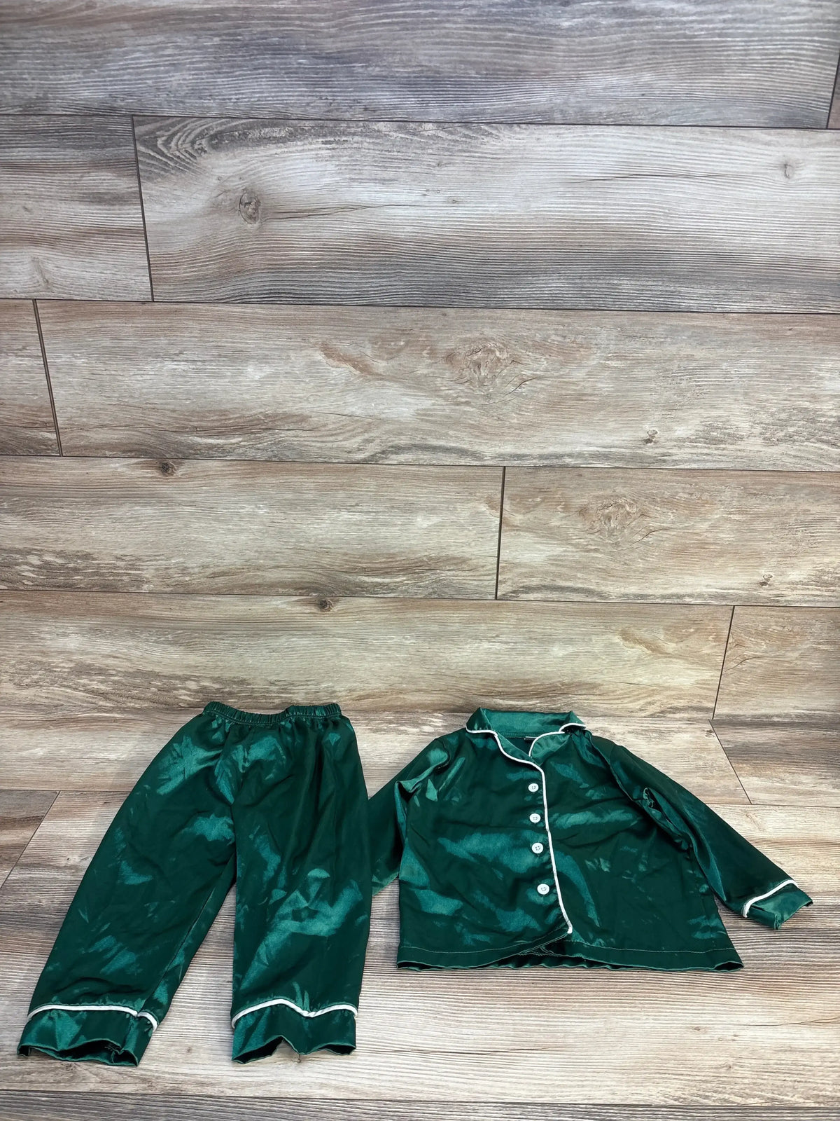 Green kids pajama set with white trim, button-front top and elastic waist pants on wood floor