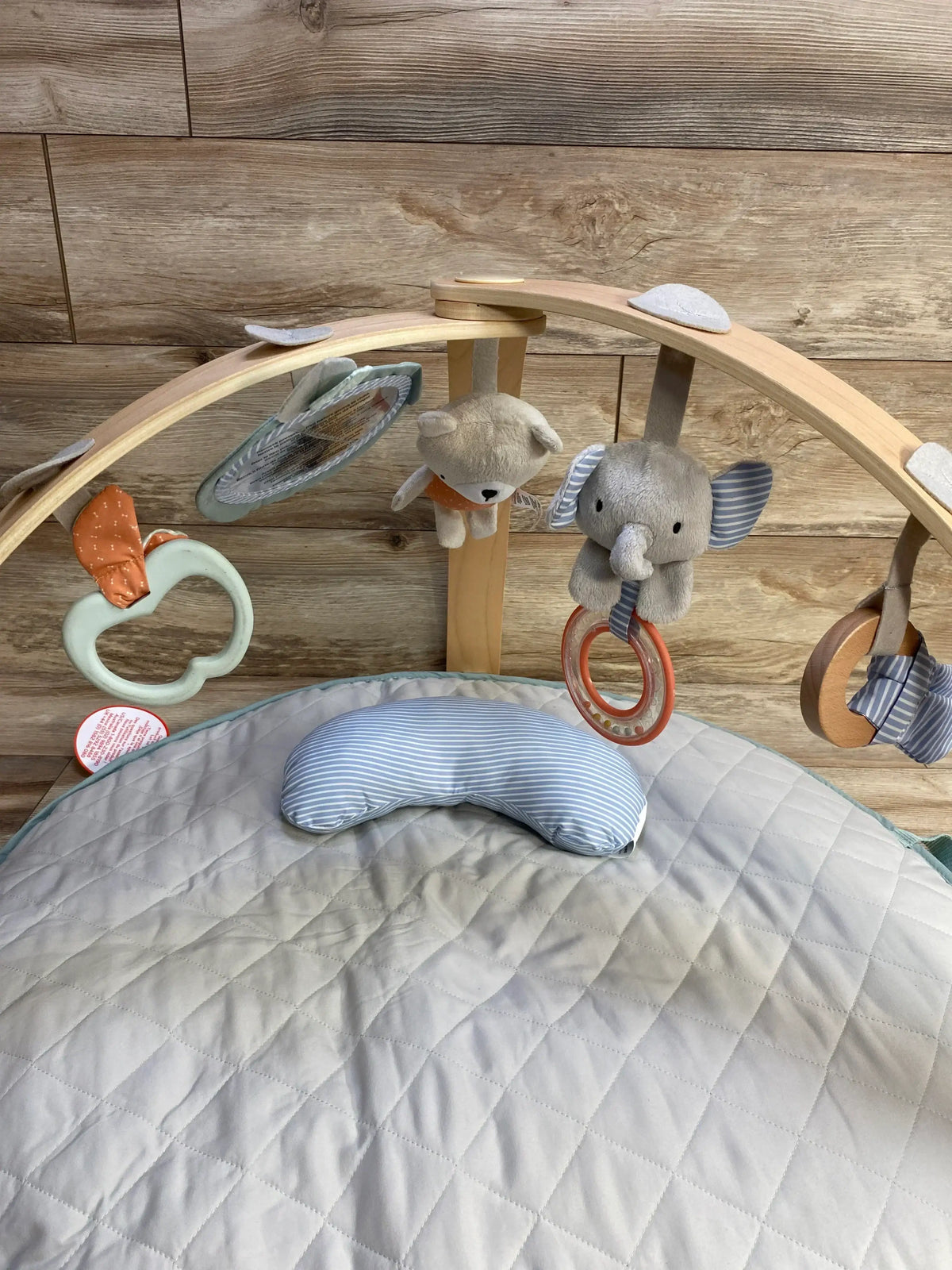 Top view of Ingenuity Cozy Spot reversible duvet activity gym showing wooden arches with hanging bear and elephant toys and quilted gray play mat