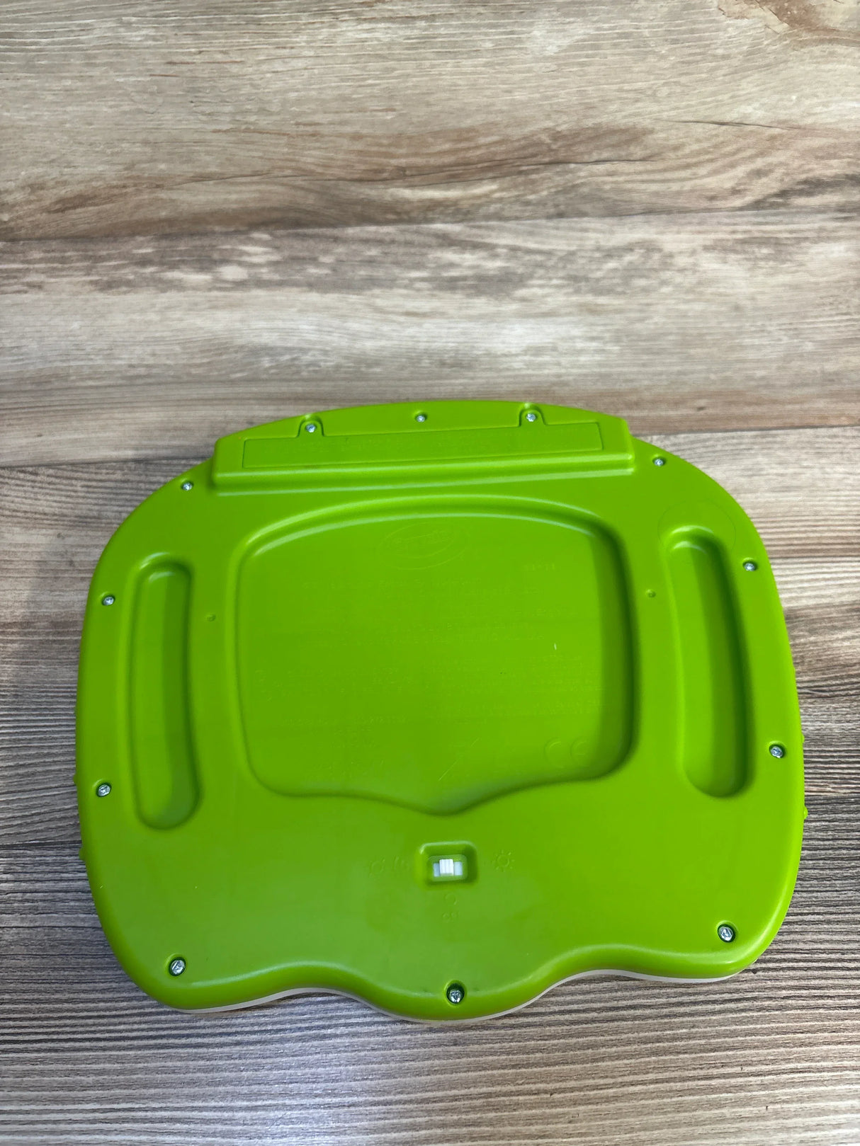 Green plastic toy base with screws and switch on wooden surface