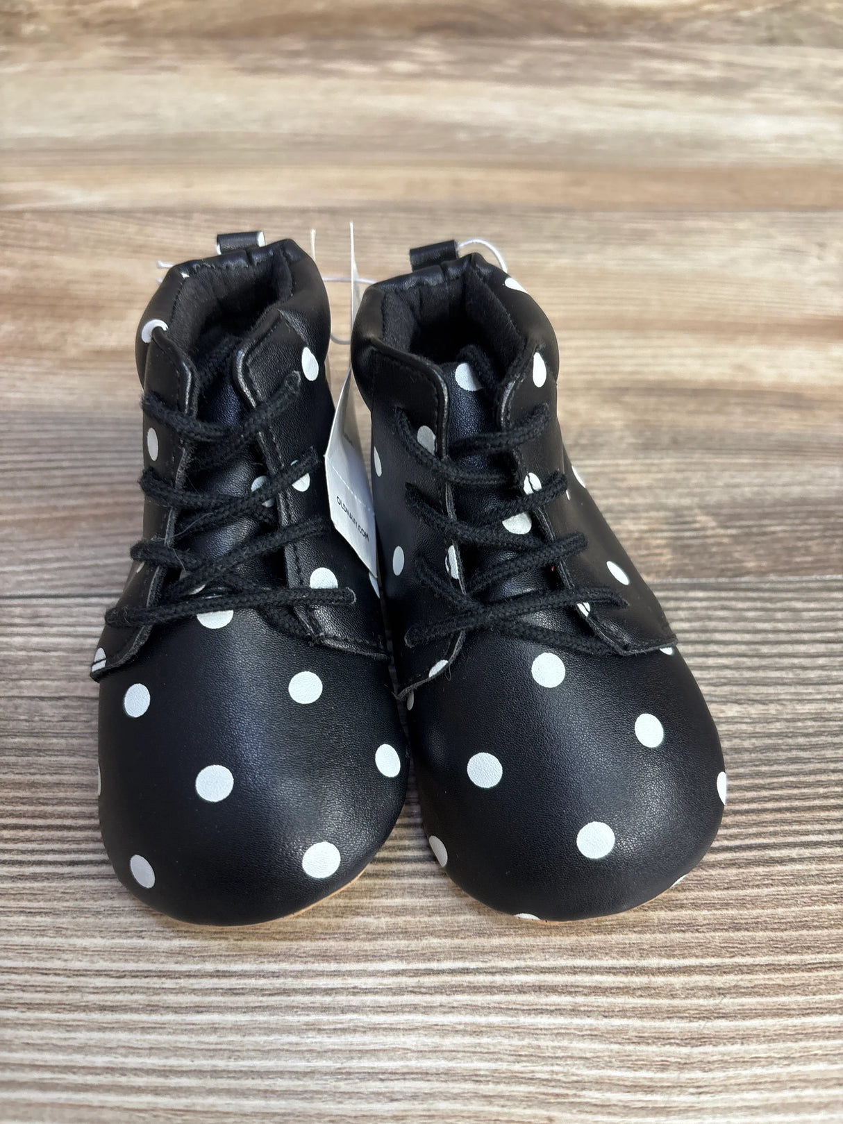 Black baby shoes with white polka dots and black laces on wooden surface