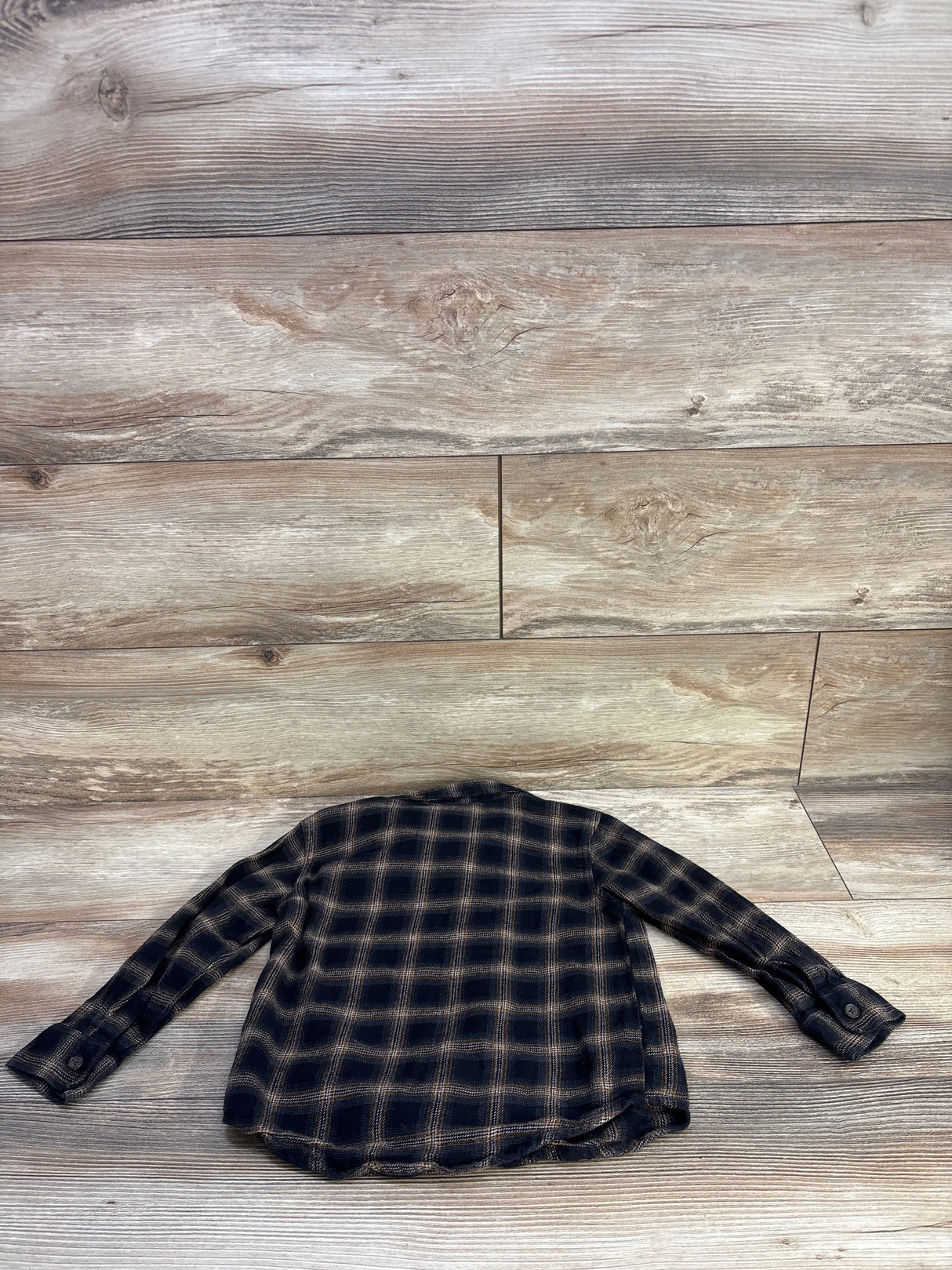 Back view of toddler black and tan plaid button-up flannel shirt showing long sleeves and curved hem on wood floor