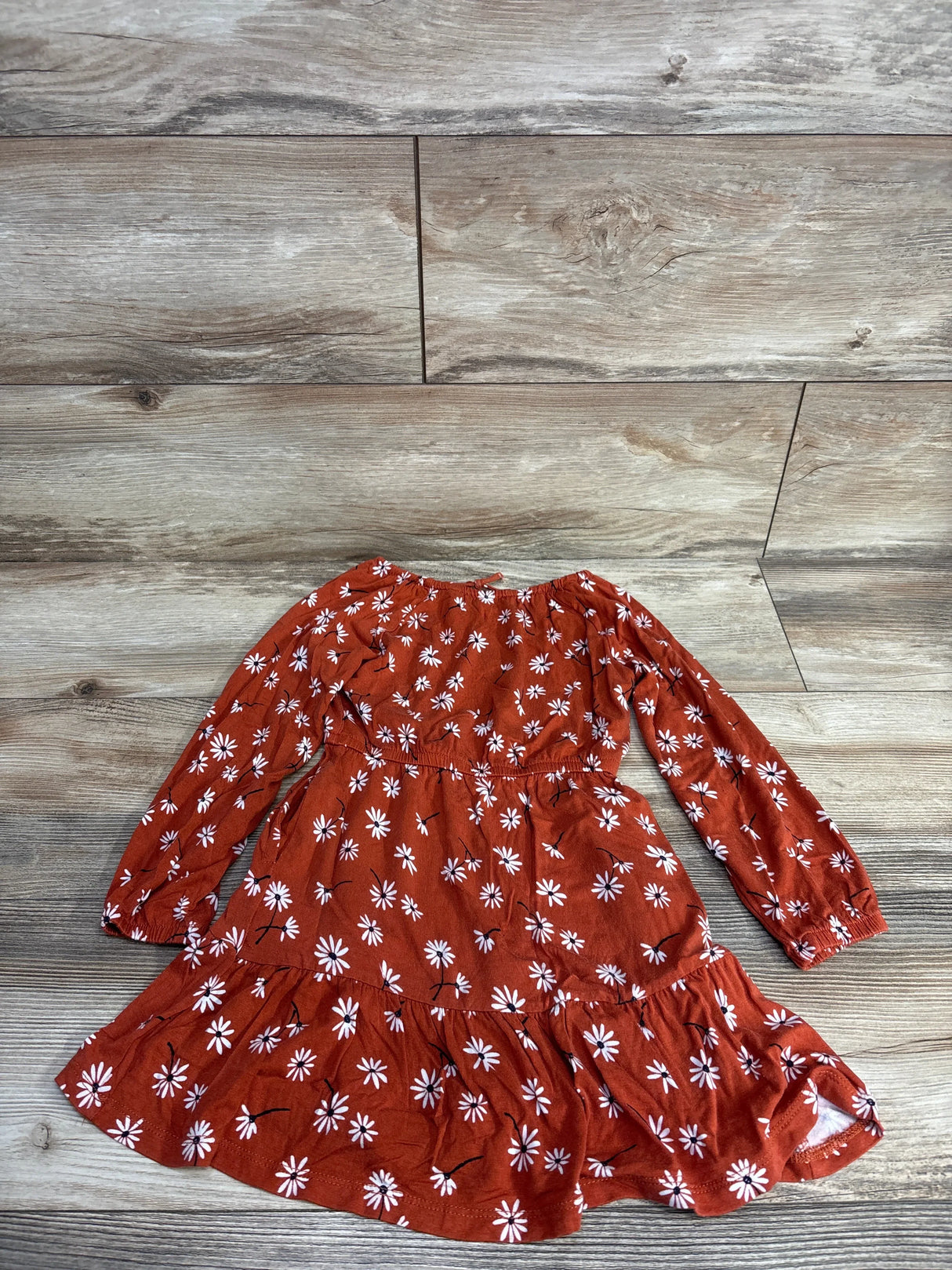 Rust orange long-sleeve toddler dress with white daisy floral print laid on wooden floor