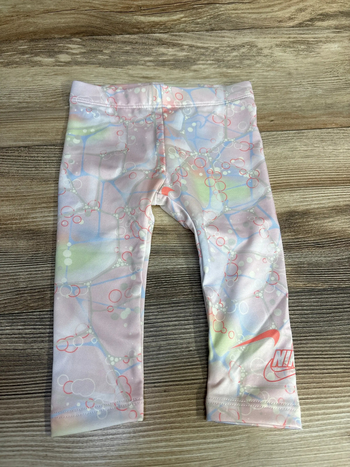 Flat lay of toddler Nike leggings size 12 months, pink pastel bubble print with elastic waistband and coral swoosh at hem on wood surface