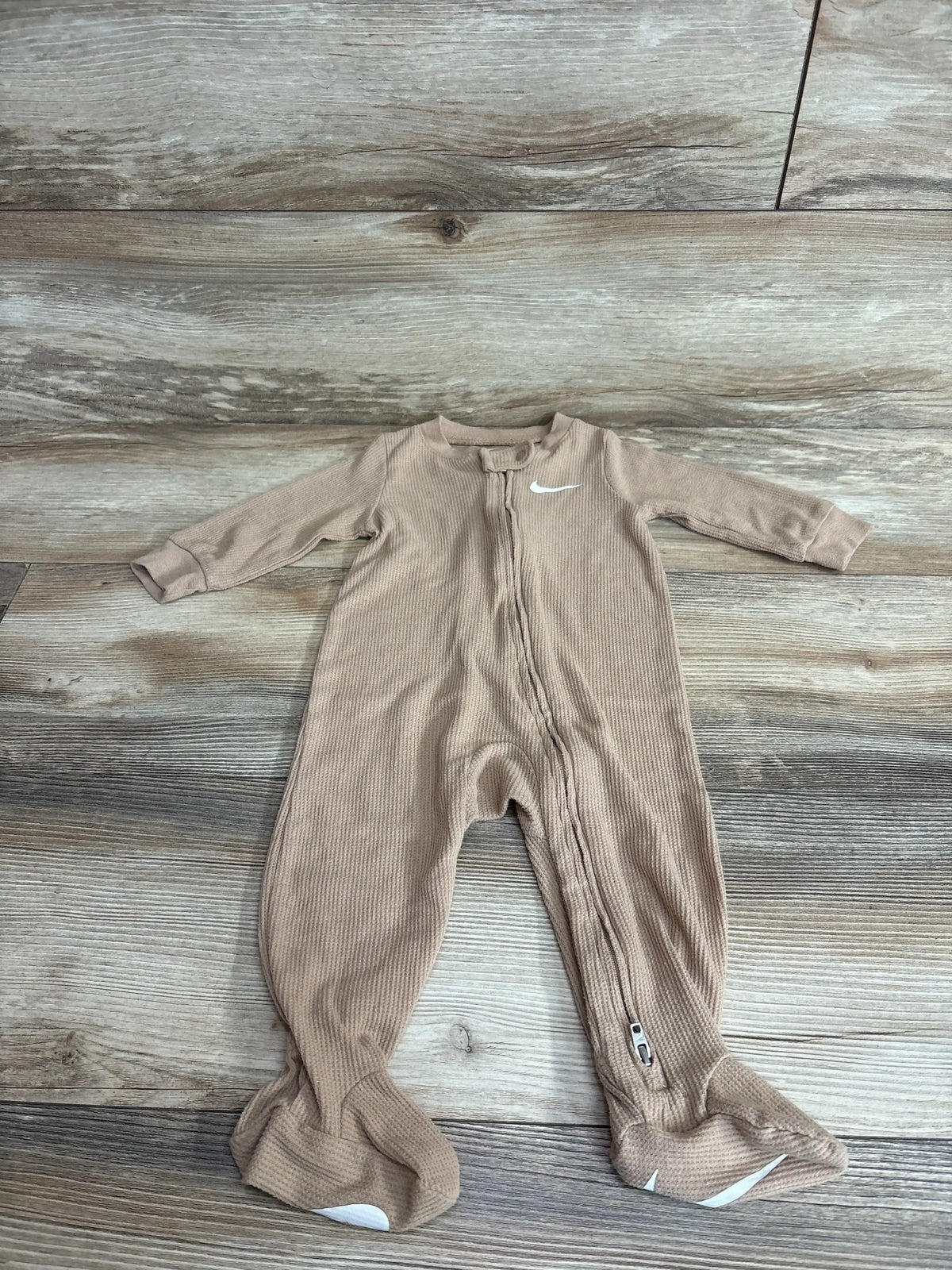 Front flat lay of tan Nike waffle knit footed sleeper size 9M with full zipper and white swoosh on wood background