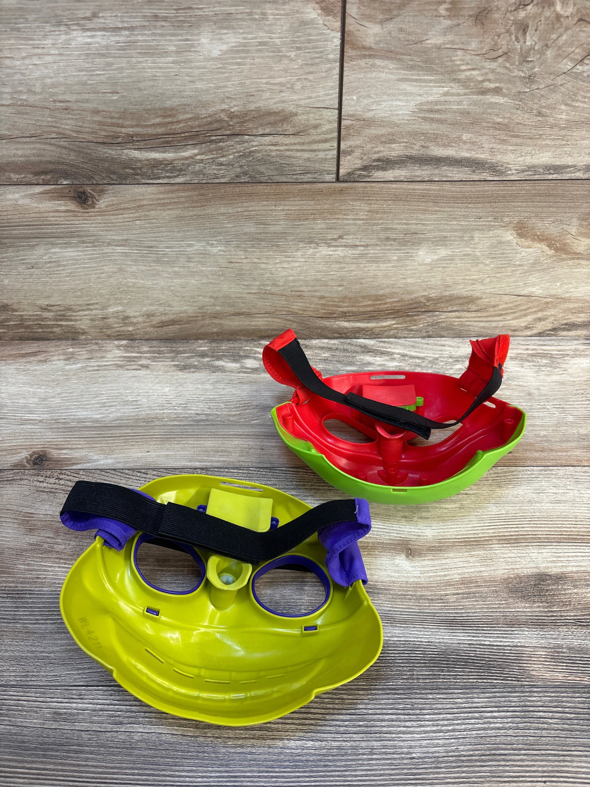 Top view of Teenage Mutant Ninja Turtles roleplay masks (Raphael red, Donatello purple) with elastic straps on wood floor
