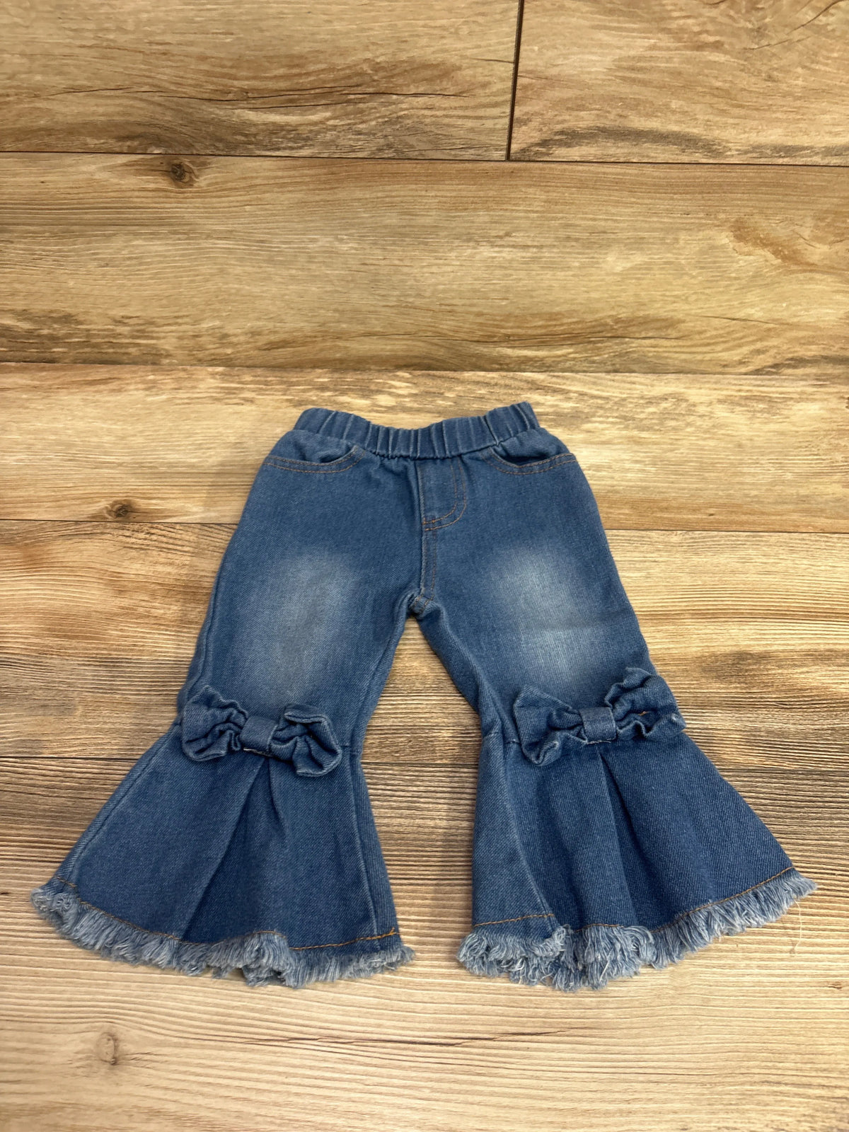 Front view of Psainyal blue bell bottom jeans, size 6-12m, with ruffled knees and frayed hems on wood flooring