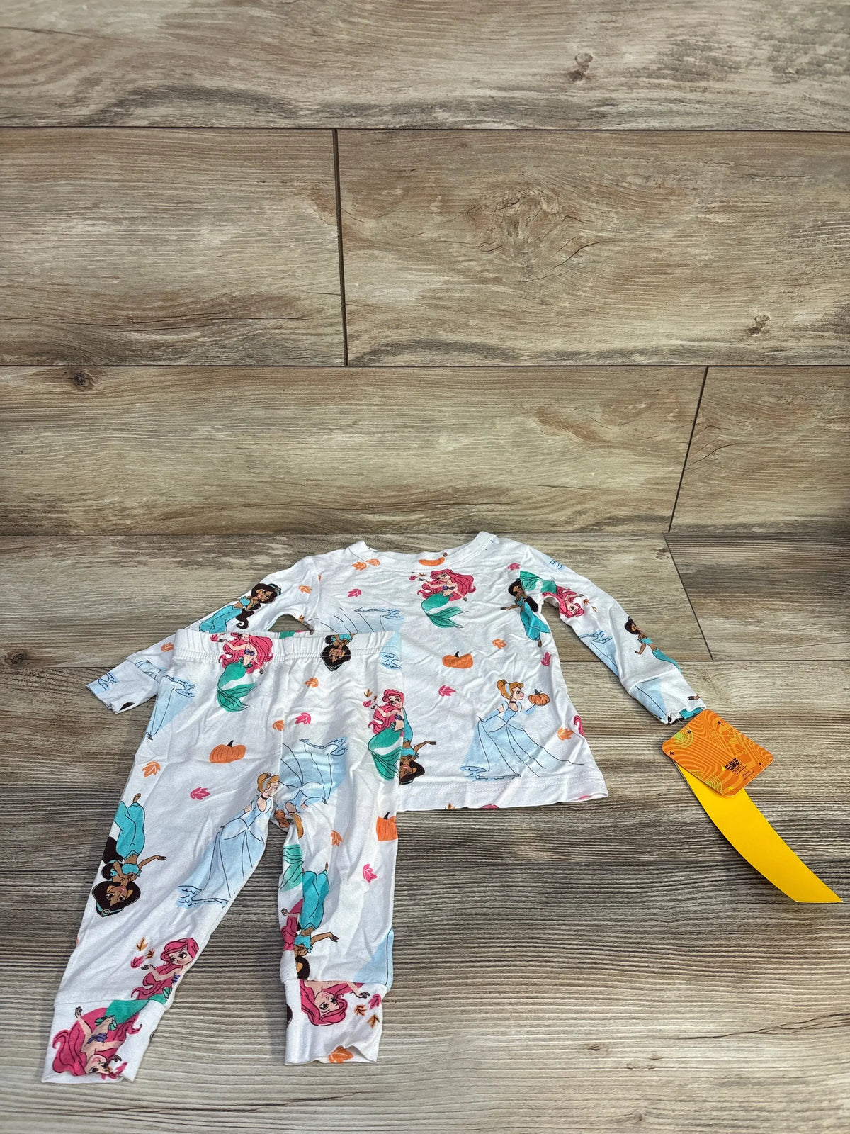 Front view of Disney Princess two piece snug fit pajamas with long sleeves and character print on a wood look floor