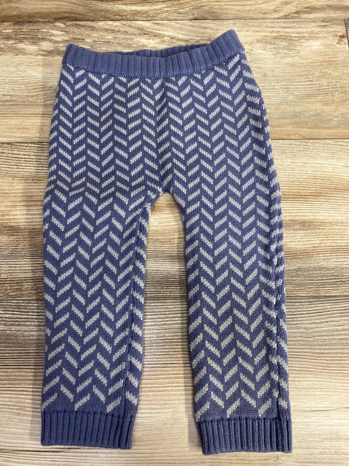 Blue knitted baby leggings with white chevron pattern on wooden background