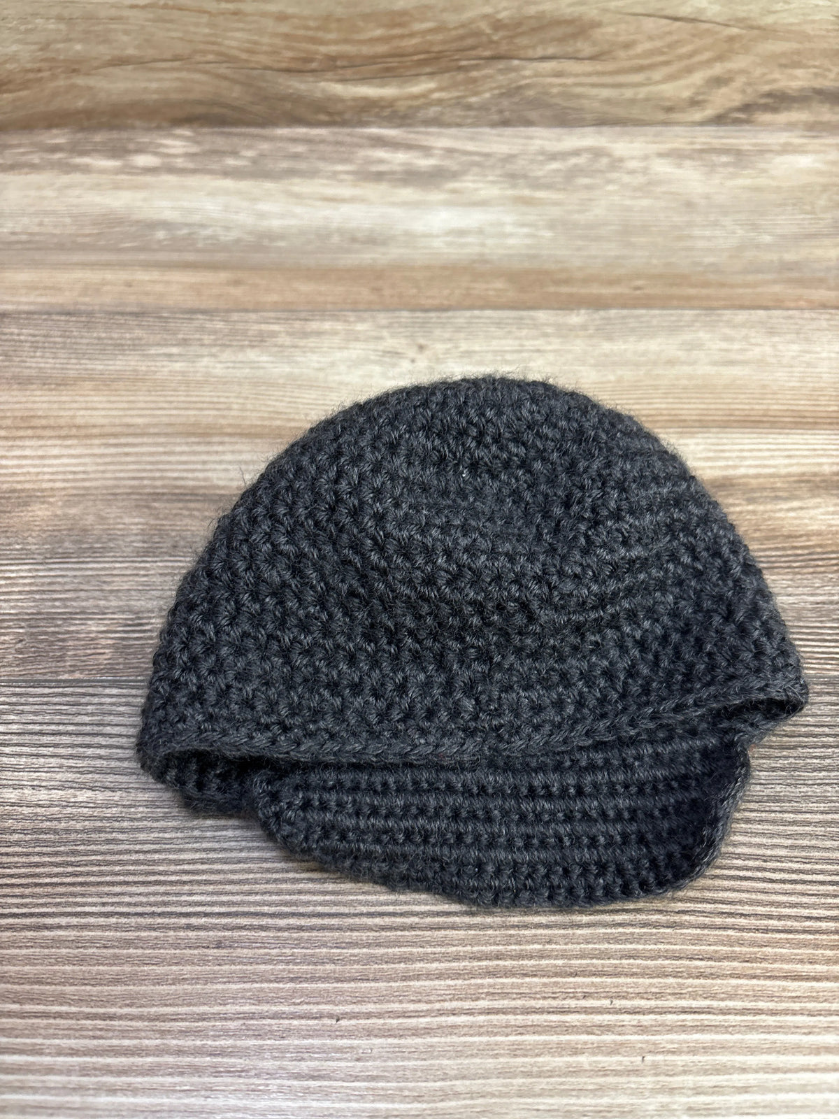 Front view of handmade crochet newborn hat showcasing grey crochet texture with a wood-grain background