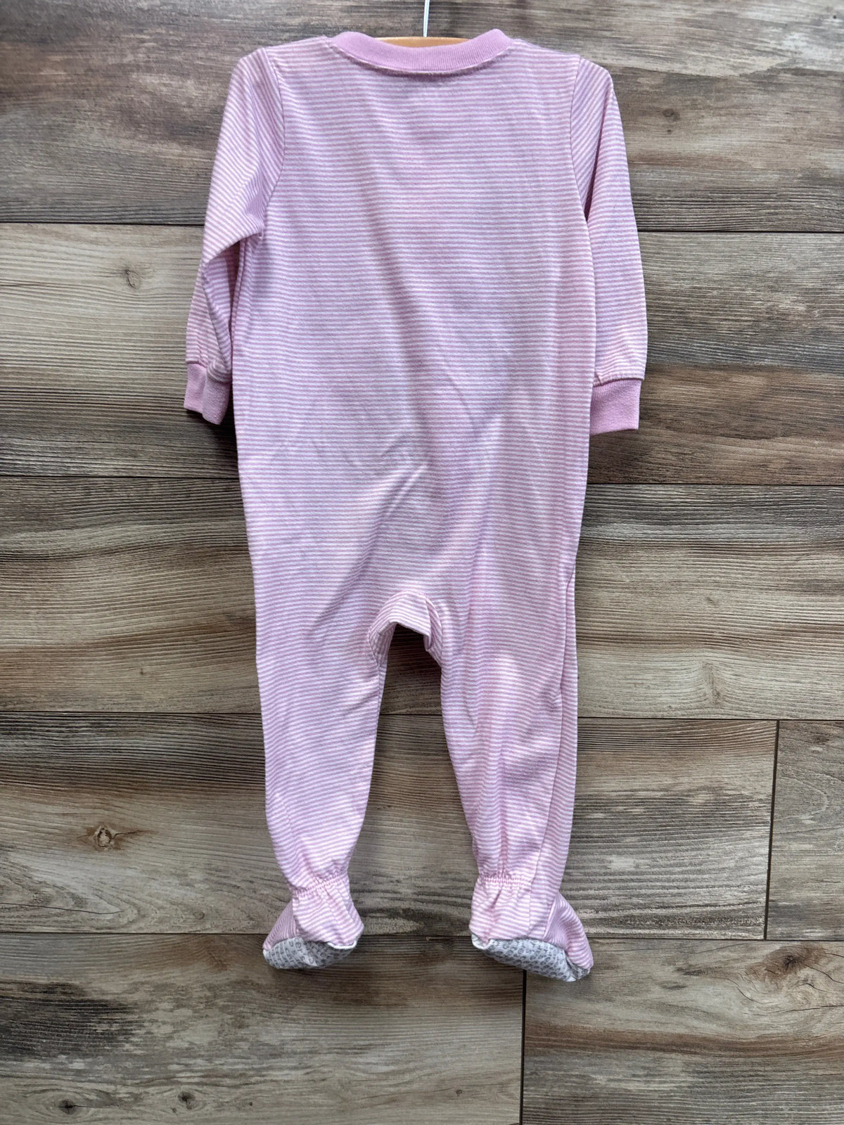 Flat lay of Just One You pink striped flamingo sleeper showcasing long sleeves and enclosed feet on a wood-grain floor
