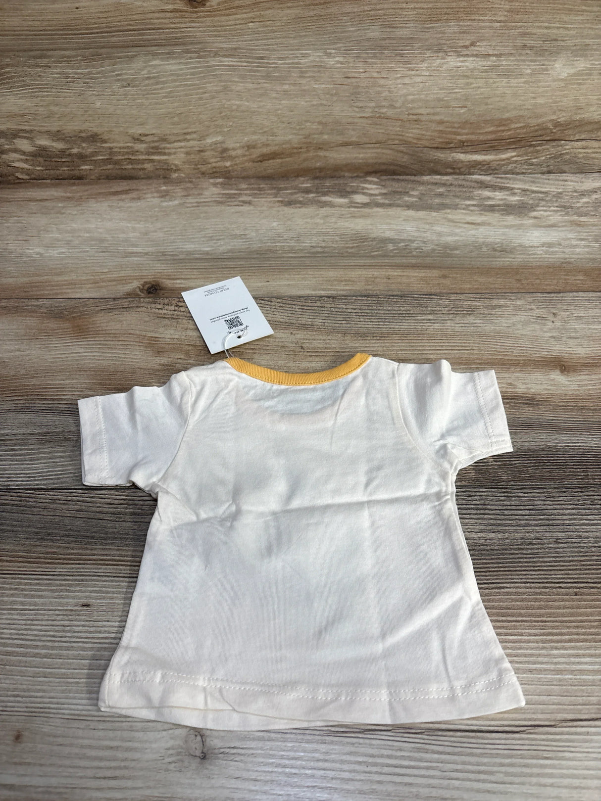 Small white cotton T-shirt with yellow collar on wooden background, clothing tag visible
