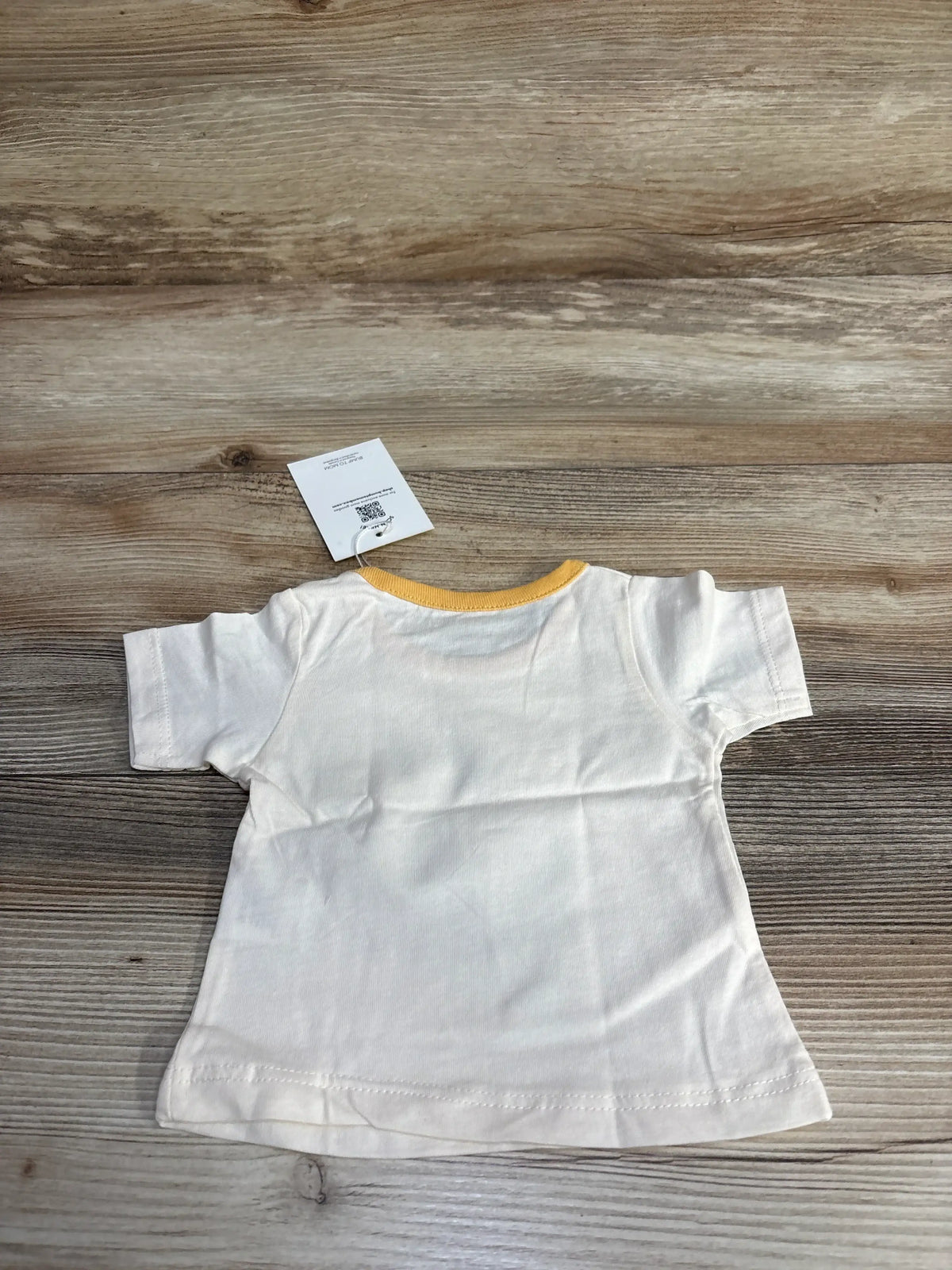 Small white cotton T-shirt with yellow collar on wooden background, clothing tag visible