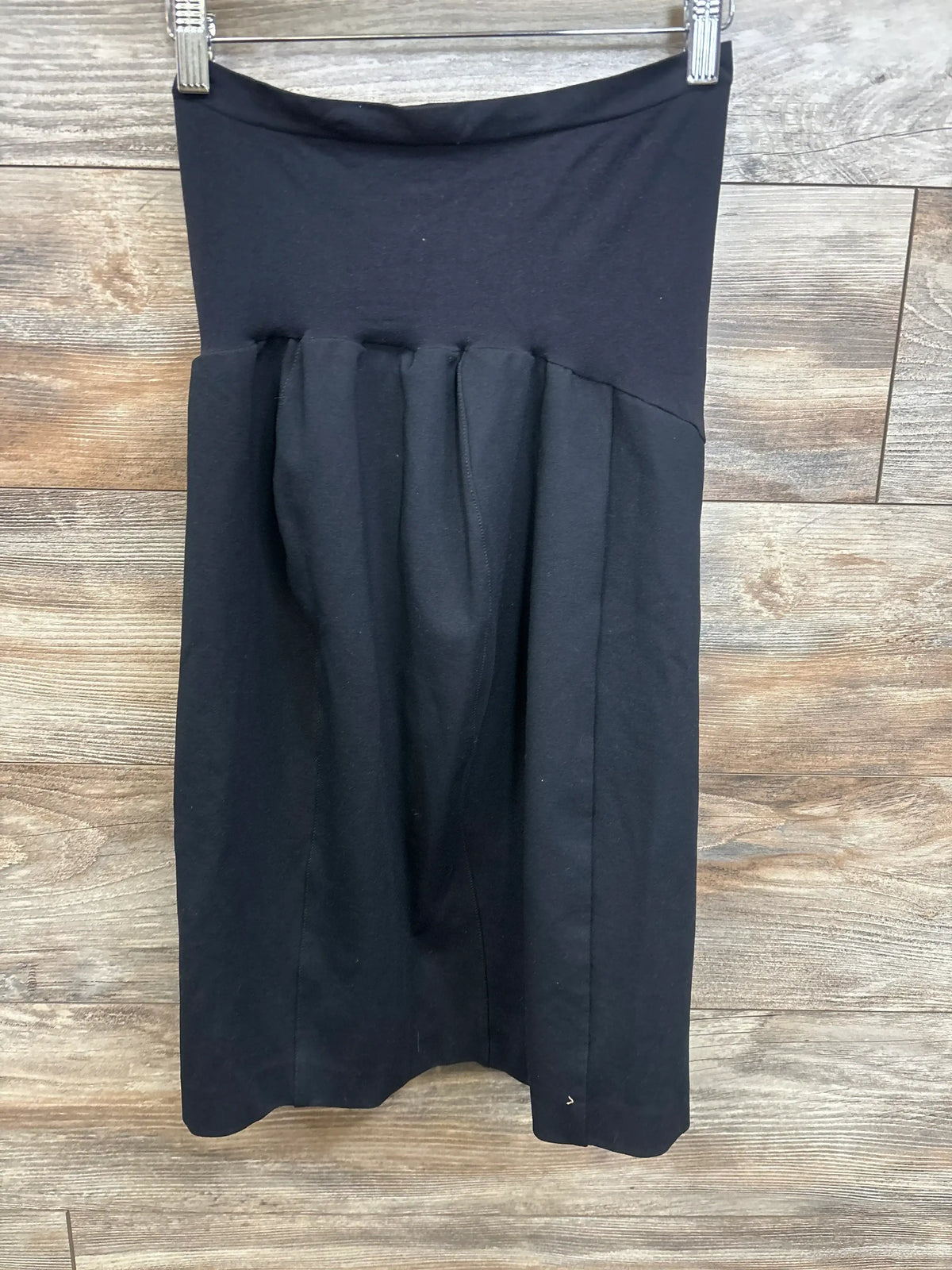Black maternity skirt with pleated detail, hanging on hanger against wood floor background