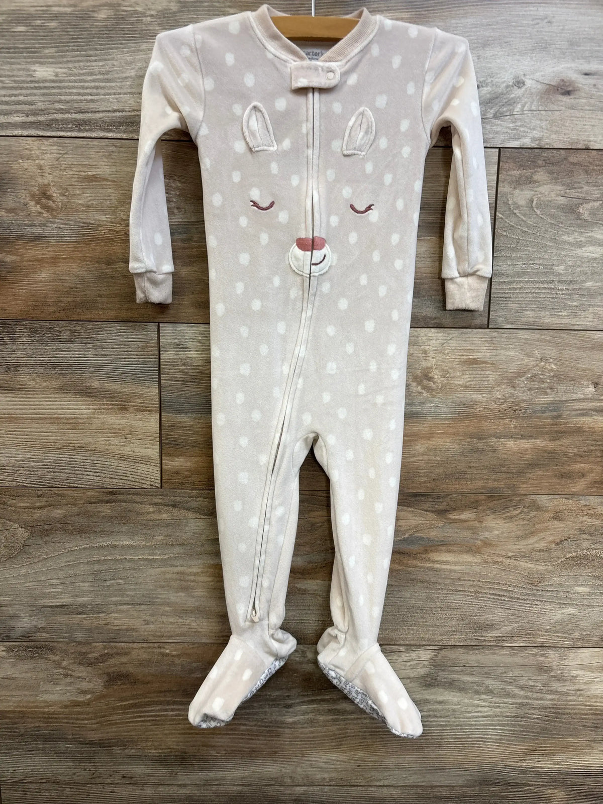 Front view of ivory Carter’s footed sleeper with zip-front, embroidered deer face and white polka dots on wood background