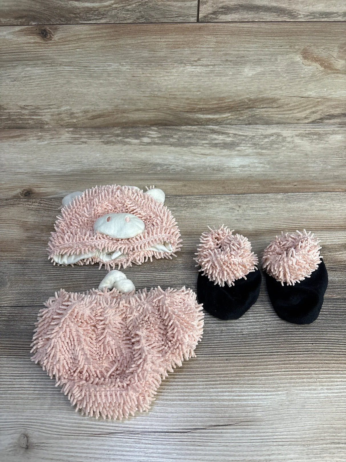 Soft pink chenille baby hat, mittens, and booties set on wood floor