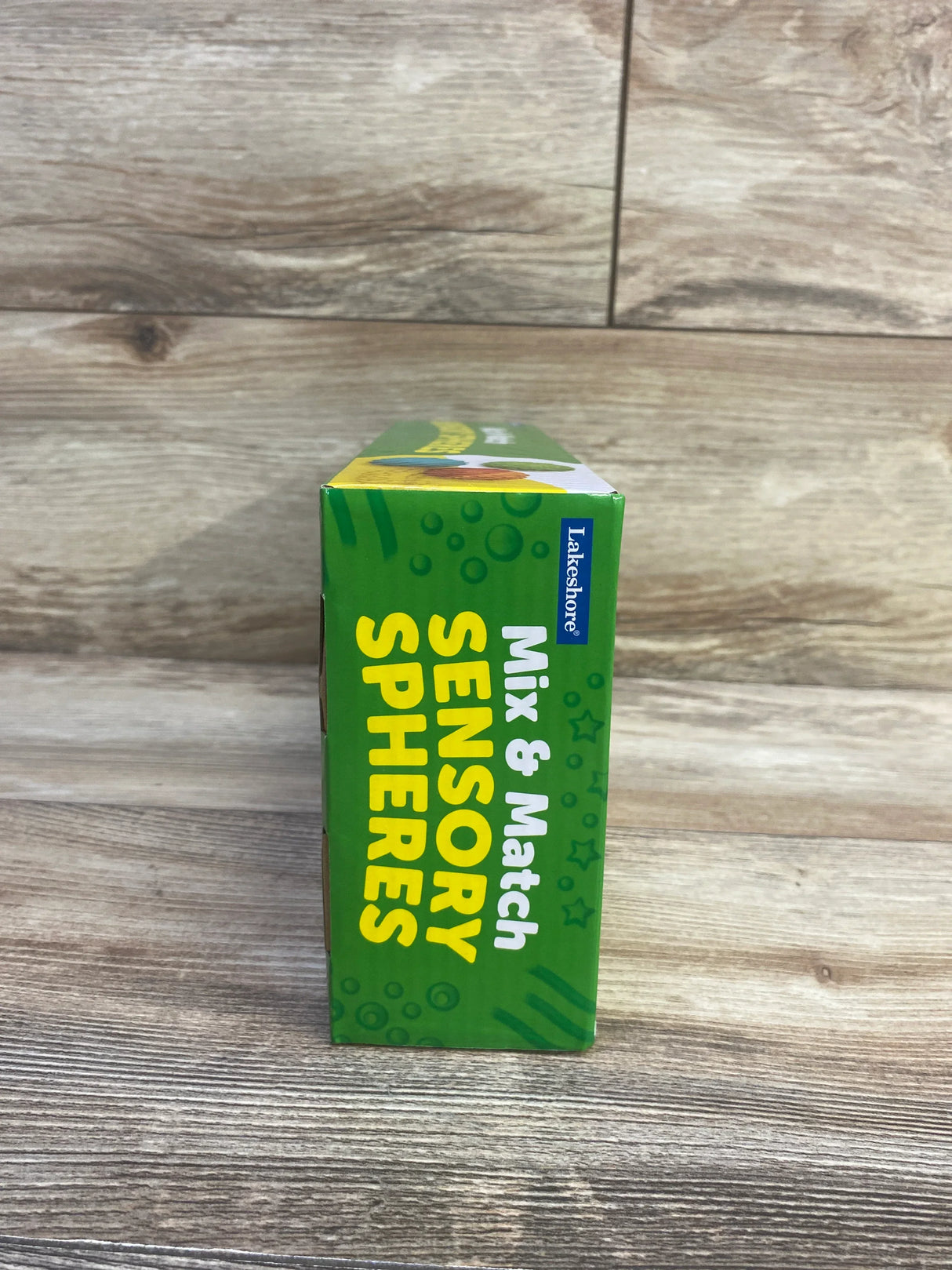 Side view of Lakeshore Mix & Match Sensory Spheres box showing product name text and Lakeshore logo on wood background