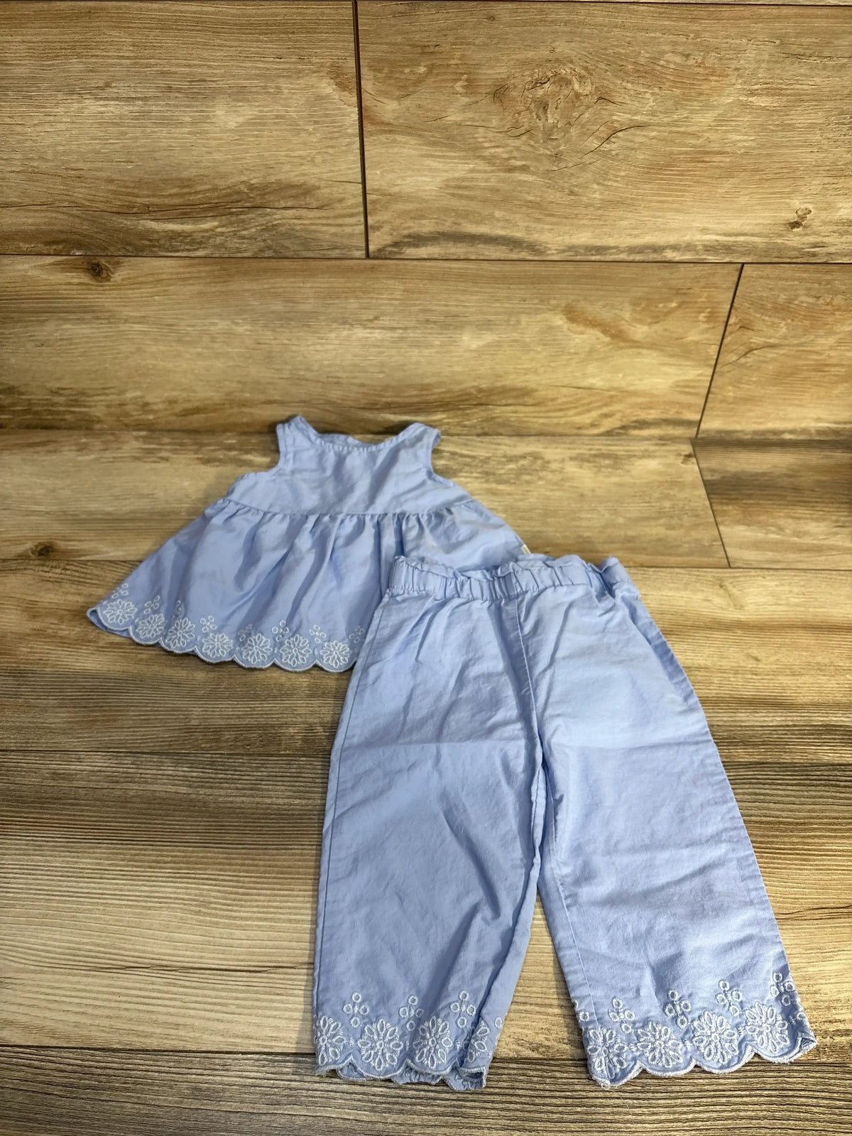 Top-down view of Tahari Baby blue two-piece set showcasing embroidered scalloped hems on top and pants, on wood