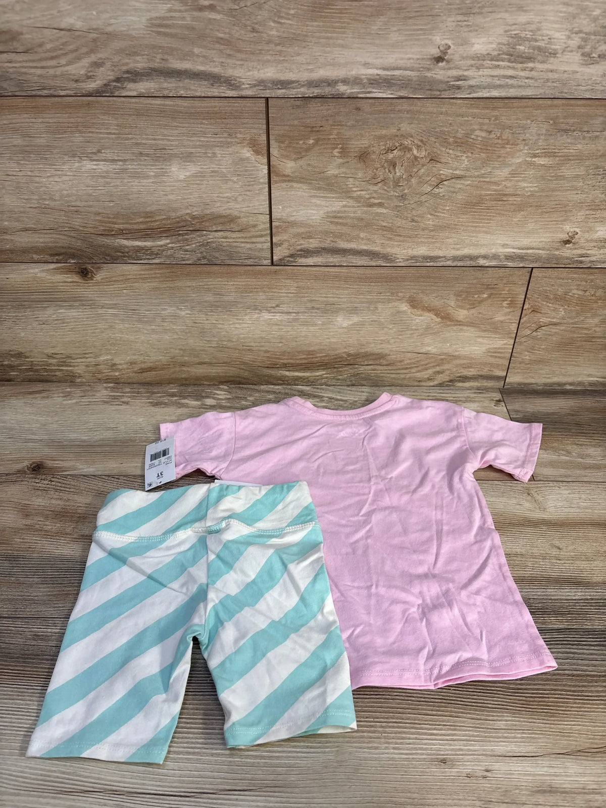 Flat lay of toddler two-piece showing pink T-shirt and mint-striped shorts on wood floor, size 3T tag visible