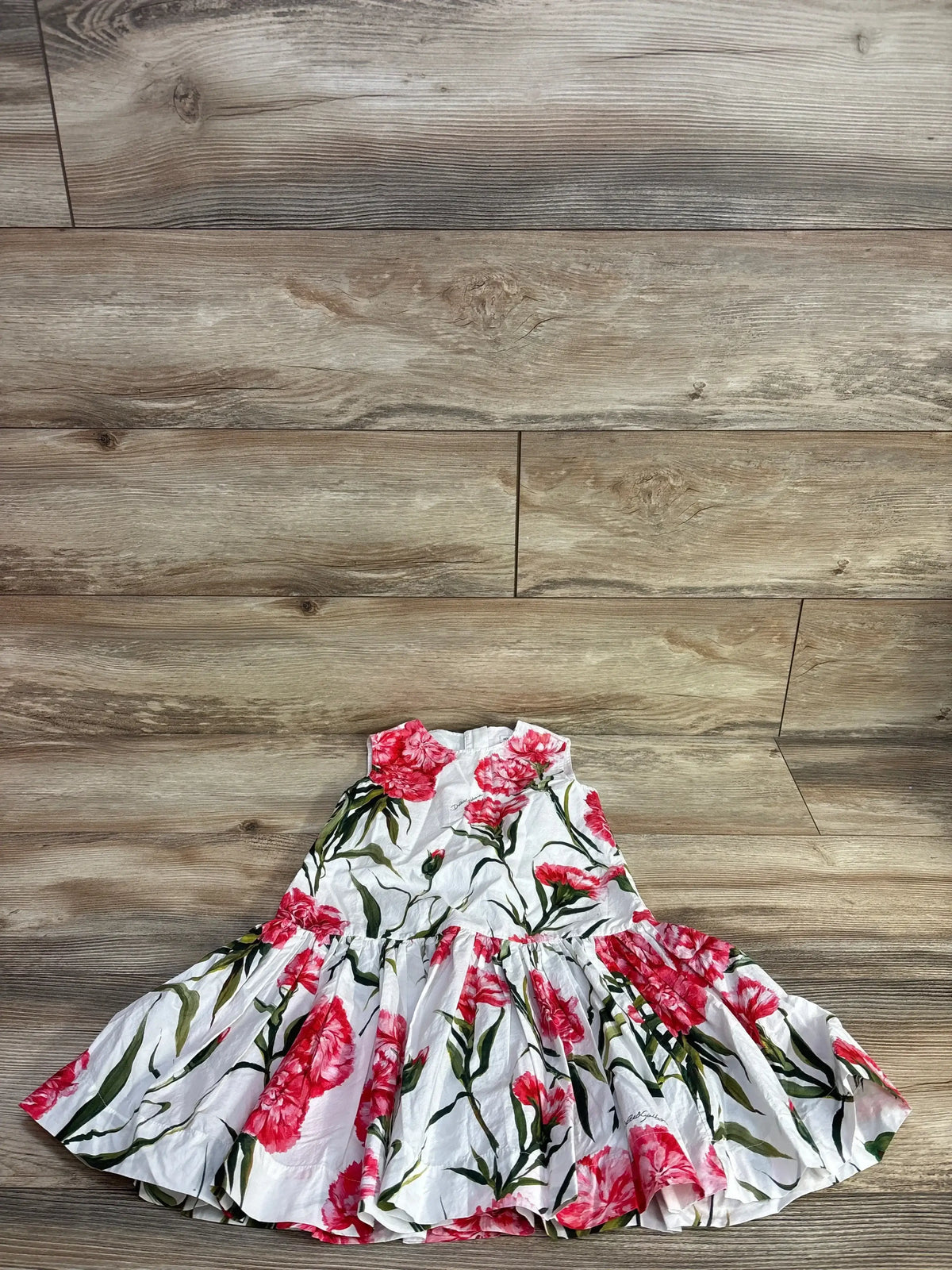 Flat lay of girls white poplin drop-waist dress with red carnation print, gathered skirt on wood floor