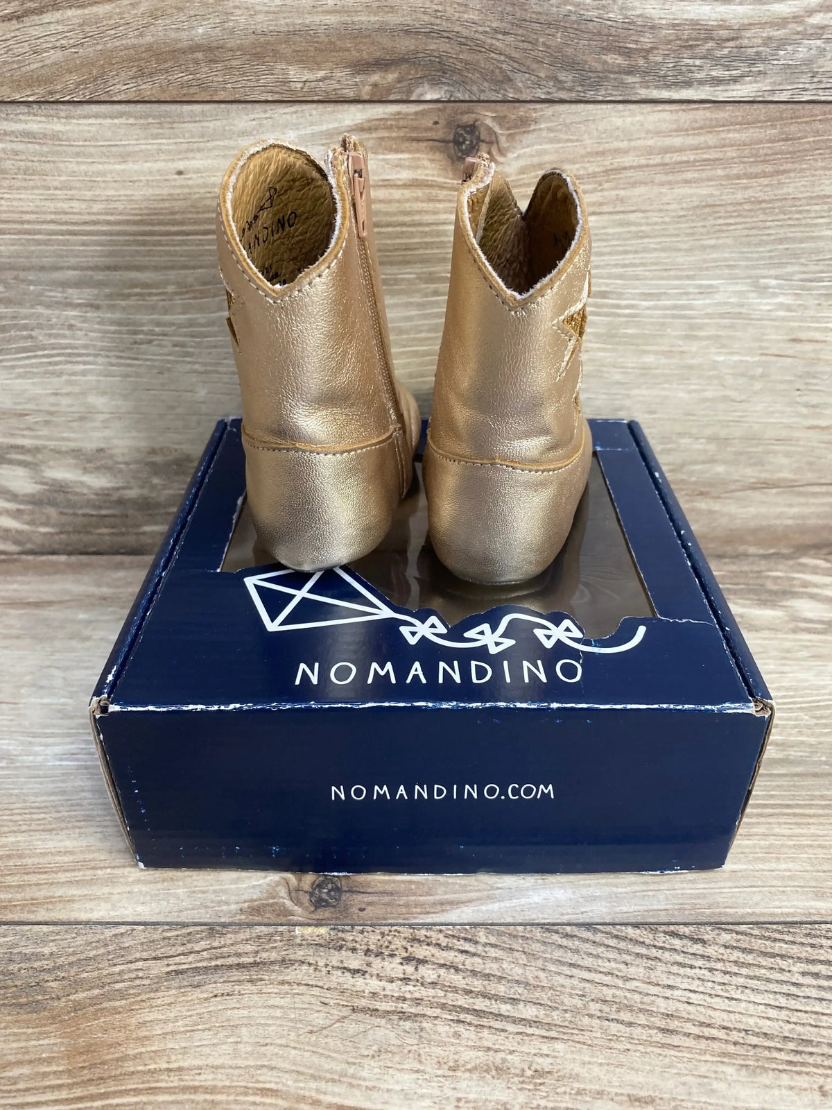 Rear view of Nomandino spark gold baby boots size 1 (3-6 months) showing star detail and side zipper on navy box with wood background