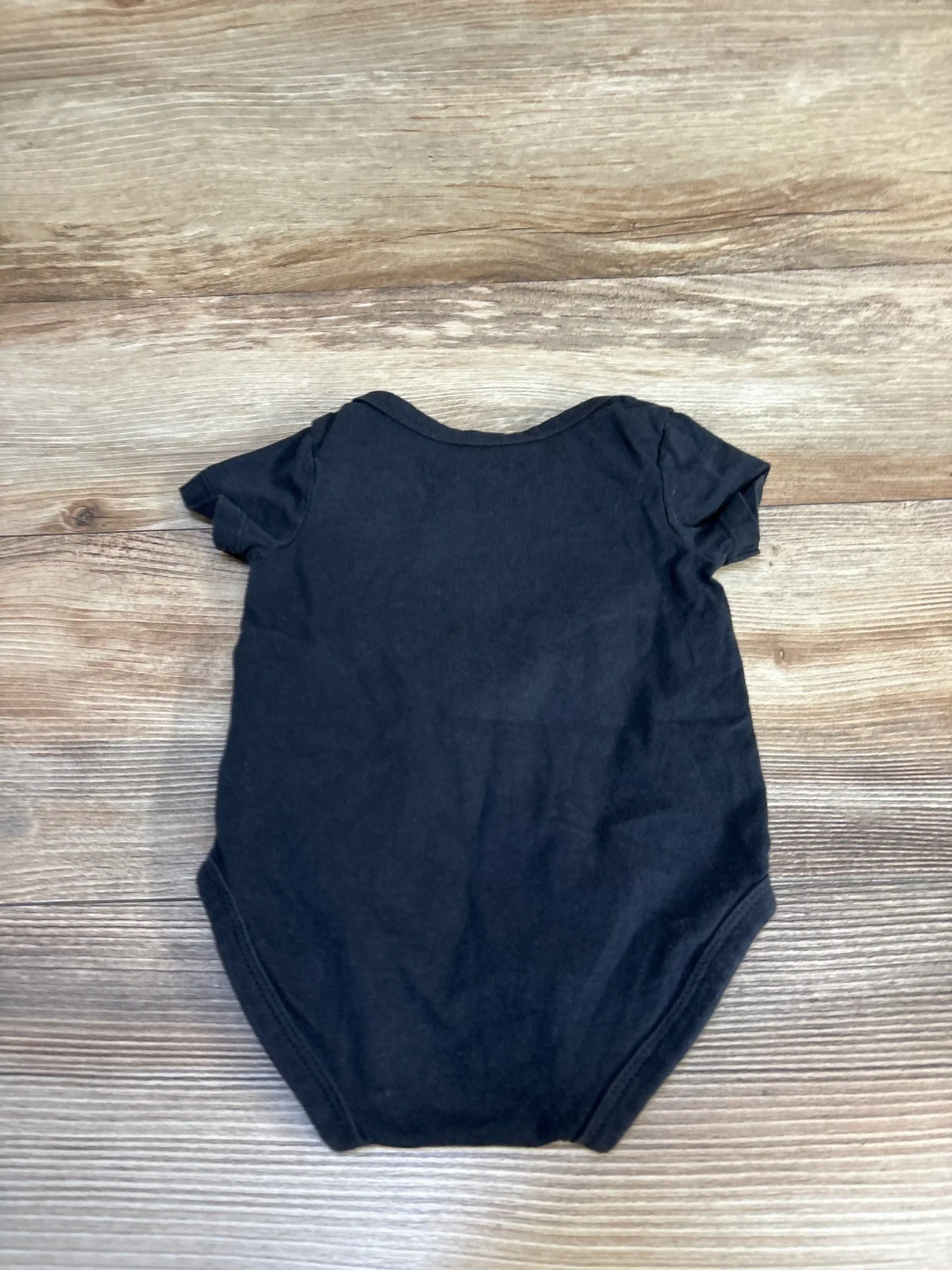 Back flat lay of Nike black baby bodysuit size 6M showing short sleeves and leg openings on wooden surface