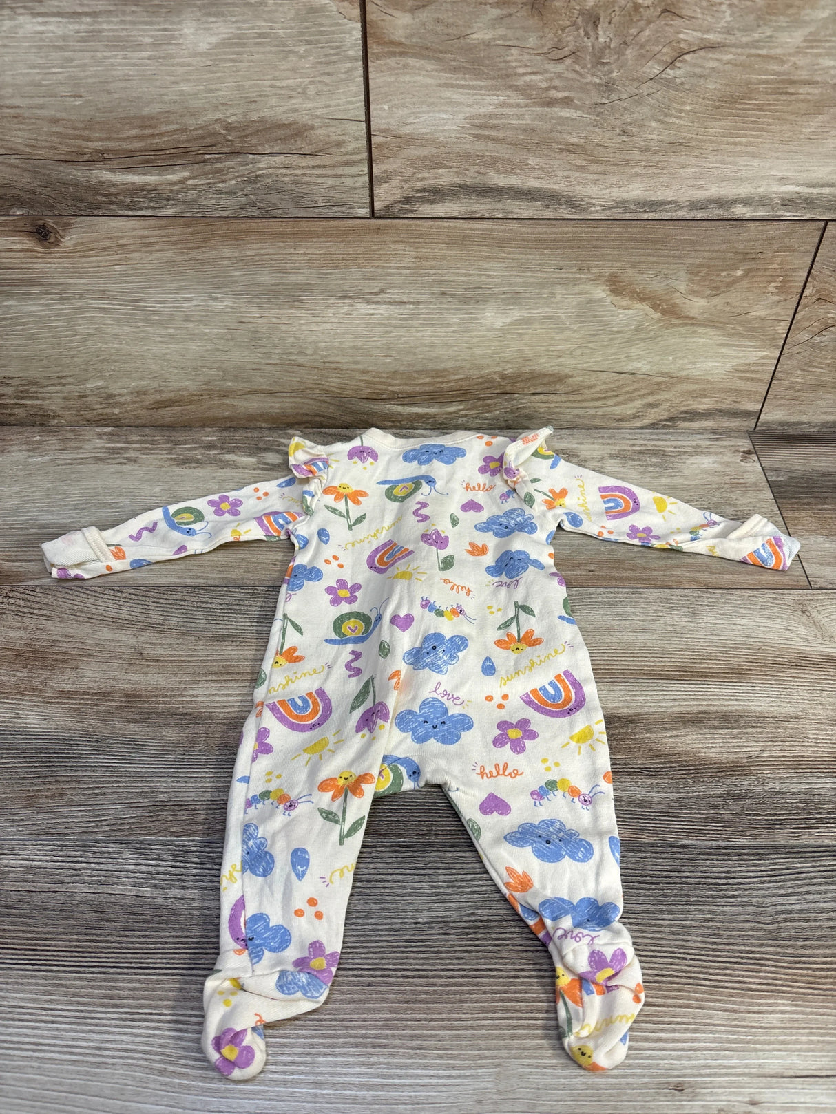 Flat-lay of Old Navy newborn 0-3M beige footed sleeper with rainbow and cloud print and ruffle shoulders on wood floor