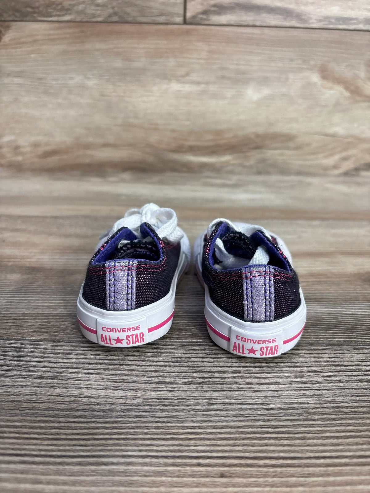 Back view of kids Converse All Star sneakers on wood floor, purple with white laces