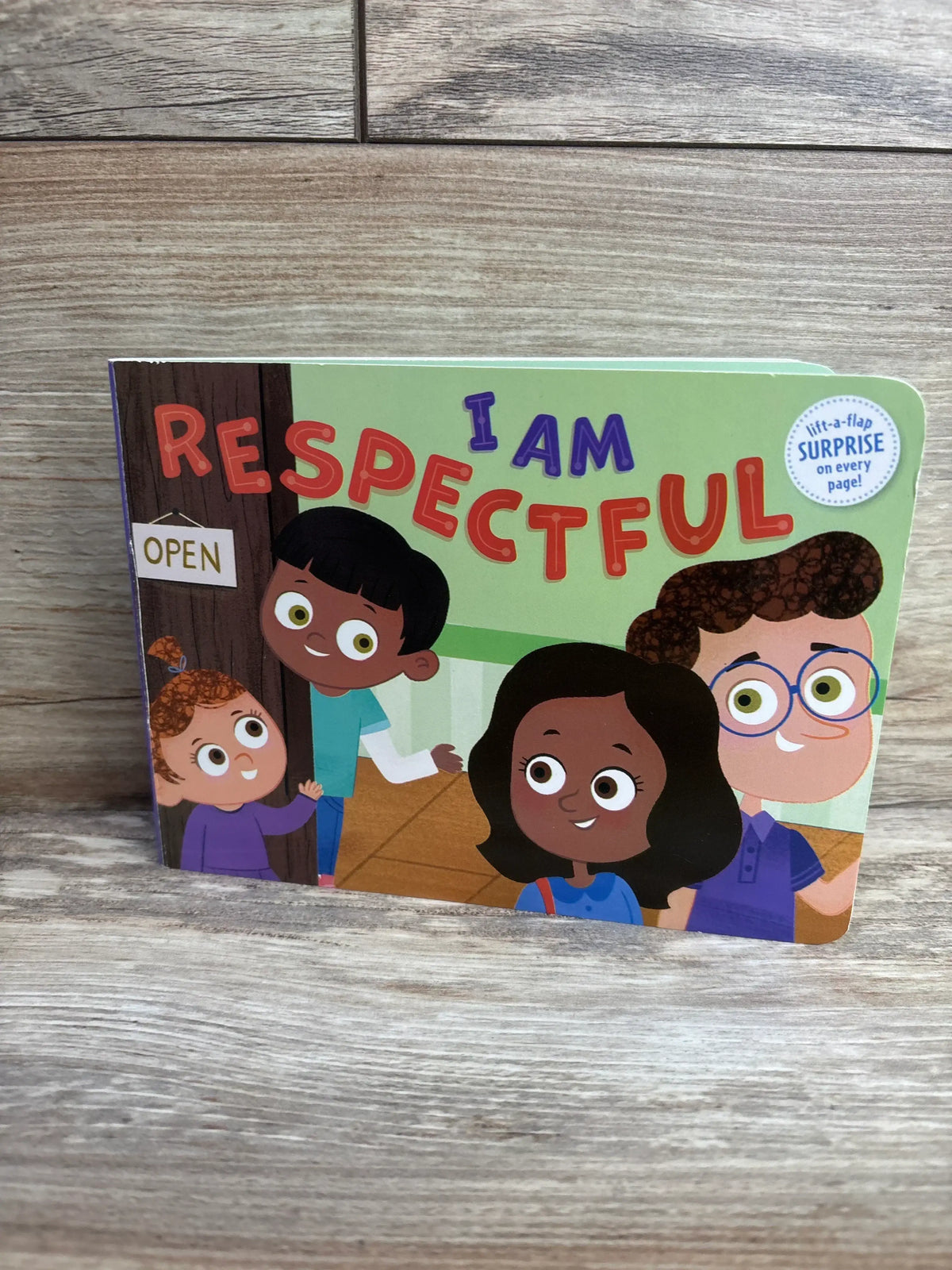 Front view of I Am Respectful lift-a-flap board book showing illustrated cover and round surprise sticker on wood background