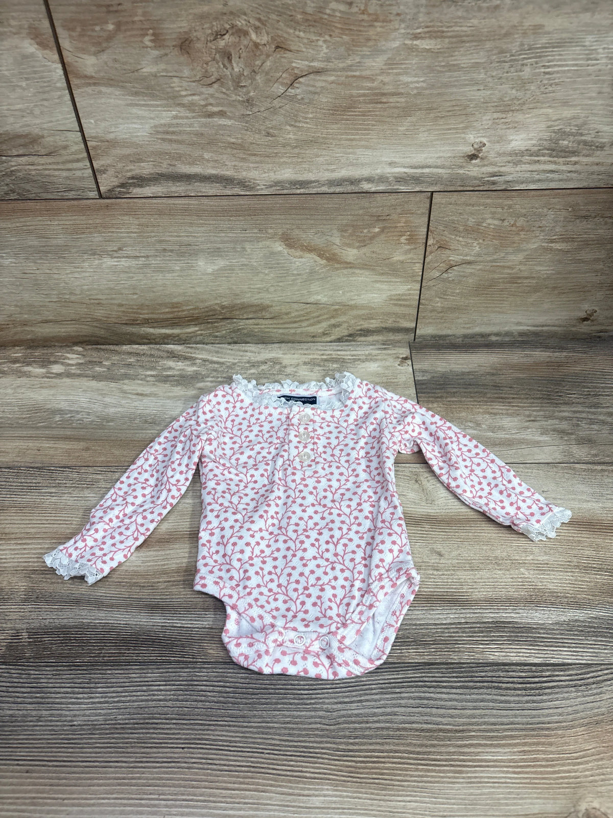Front view of French Connection white long-sleeve bodysuit with pink floral pattern and lace trim on a wood floor