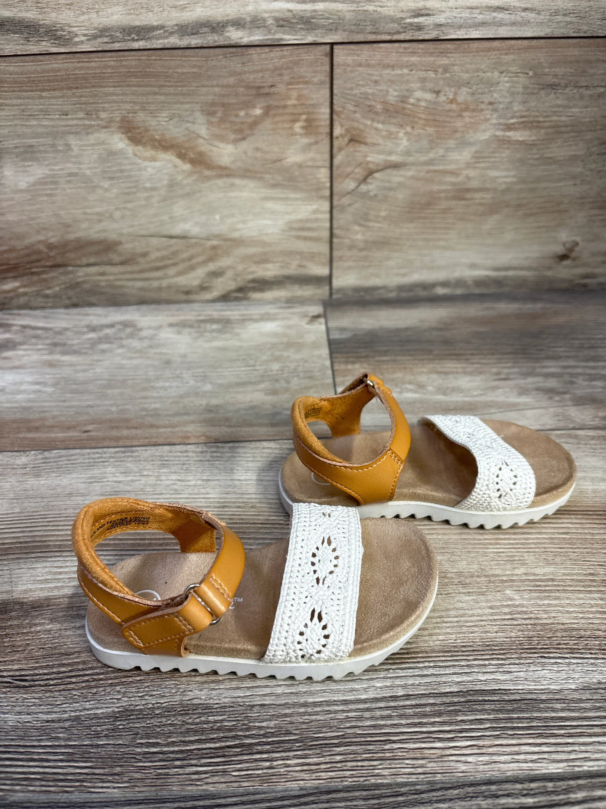 Angled top view of Cat & Jack Blair toddler sandals showing tan ankle straps and white crocheted toe bands on wood floor