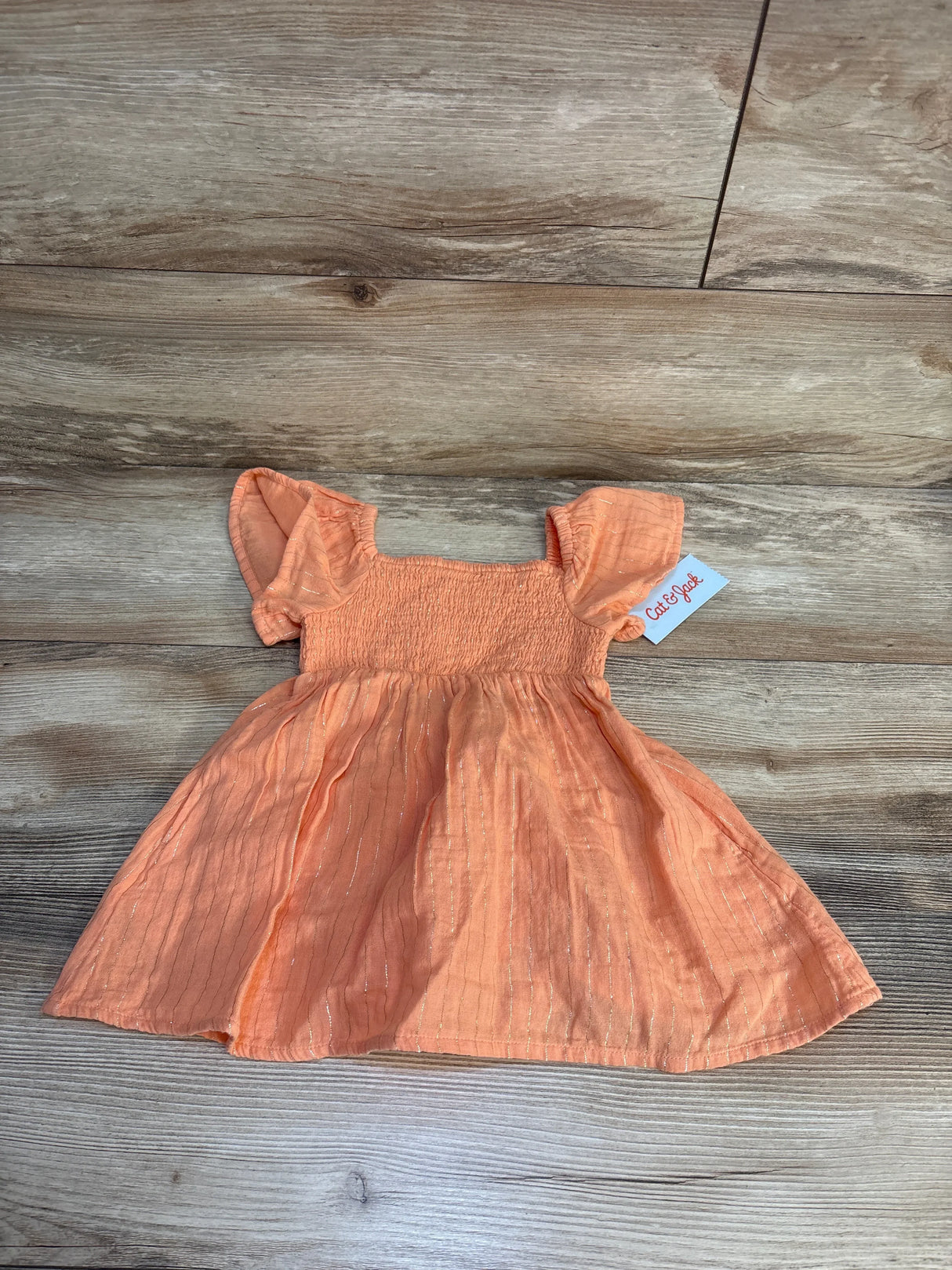 Peach short sleeve baby dress with ruffled sleeves, smocked bodice, and subtle gold shimmer